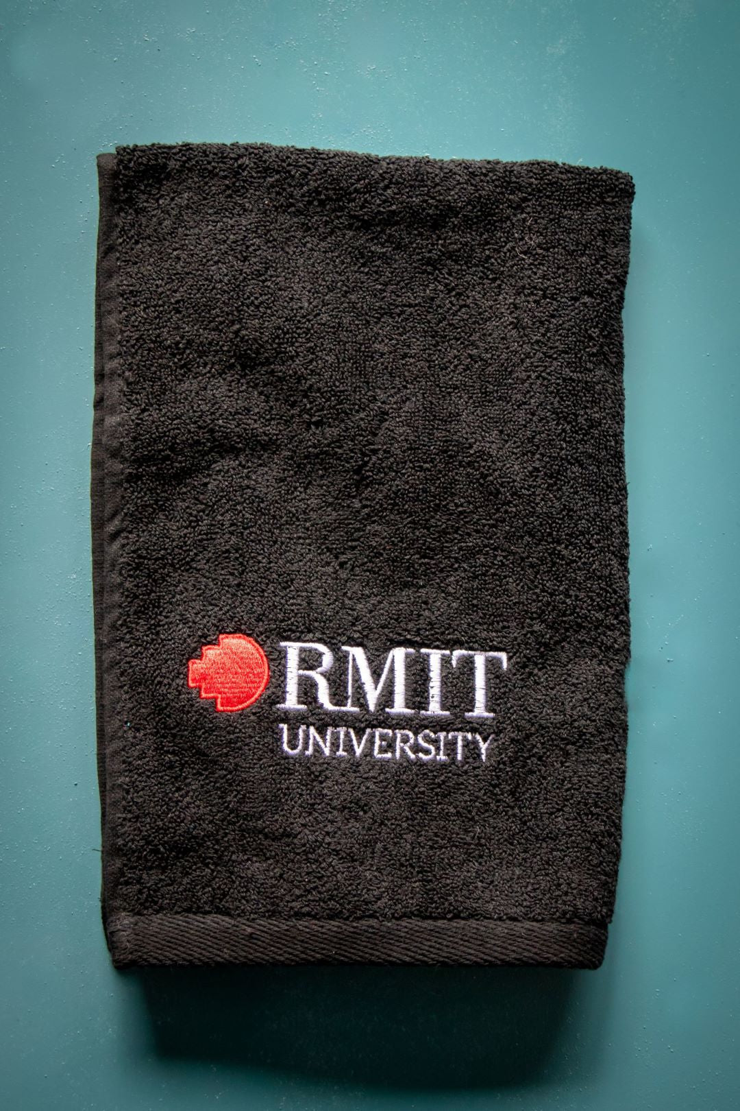 Folded RMIT Store hand towel neatly displayed with the "RMIT University" logo in white and red clearly visible on the front. 