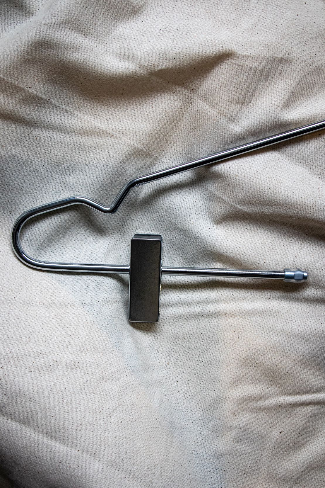 Hanger top in matte silver finish featuring a smooth, curved hook and wide contoured shoulders, shown in a close-up view resting on a beige fabric tabletop with soft lighting. Available from the RMIT Store.