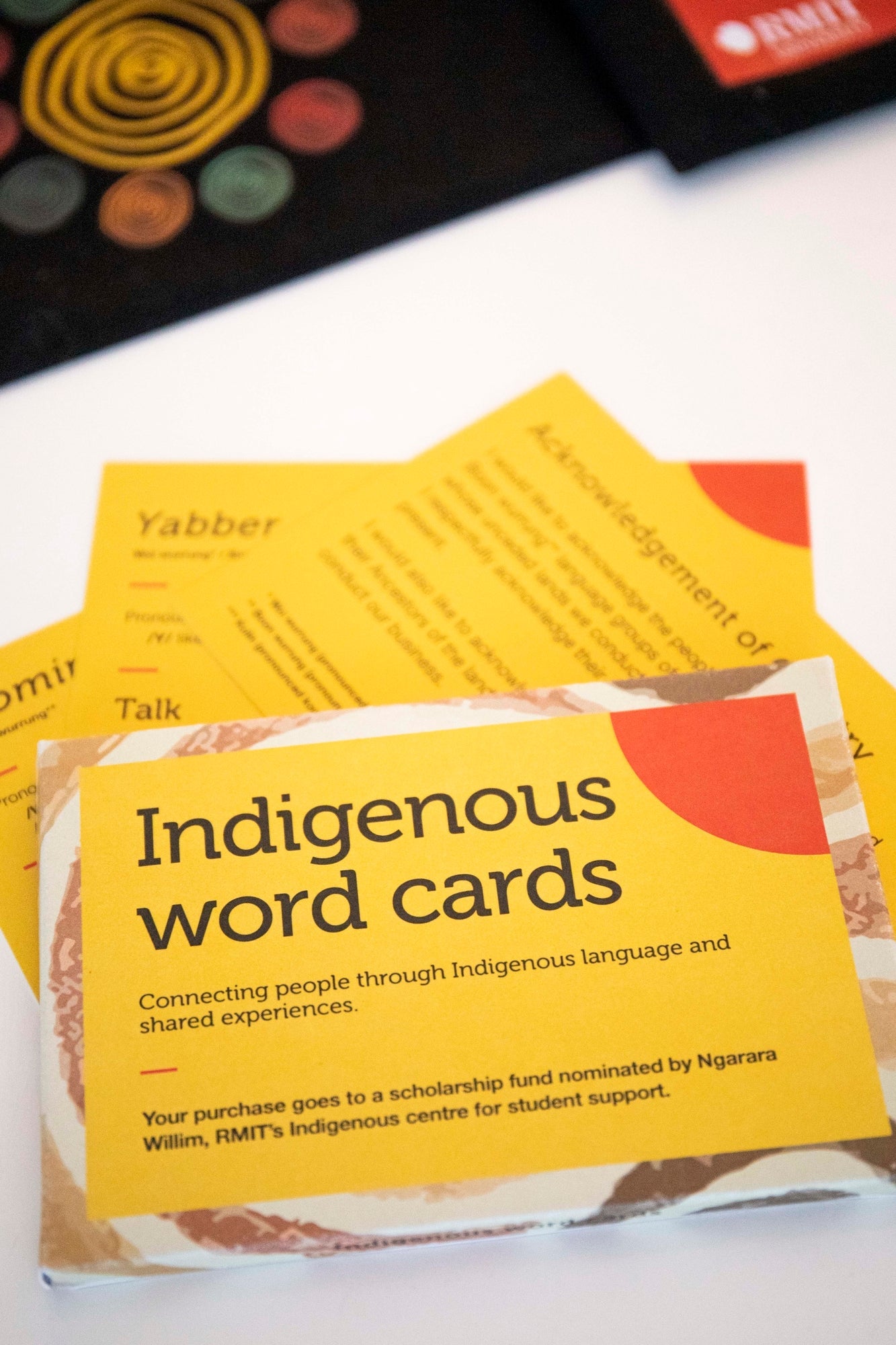 Pack of Indigenous Words Cards from the RMIT Store, shown whole and stacked on top of a white surface with three loose cards fanned out underneath. 