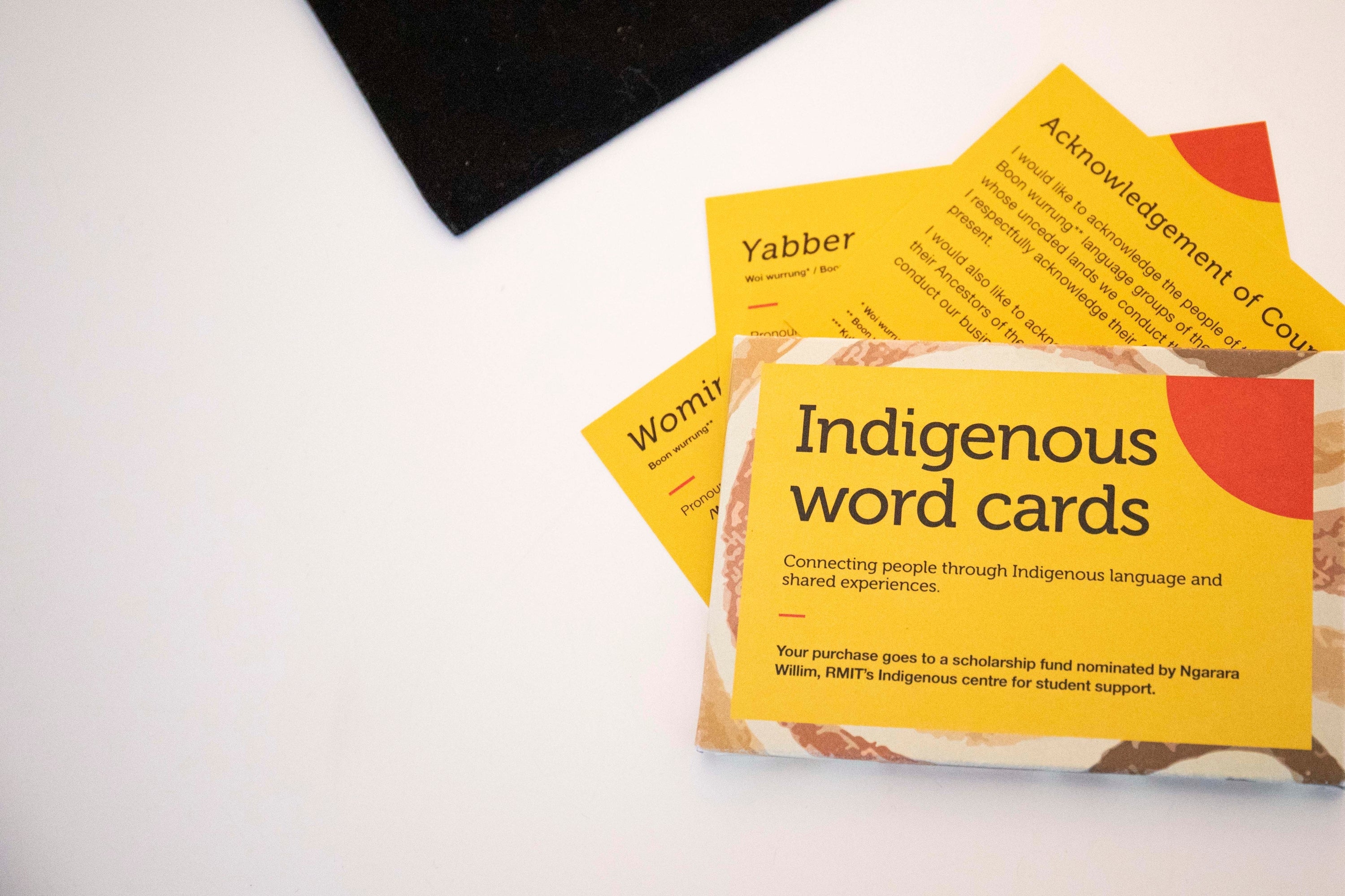 Pack of Indigenous Words Cards from the RMIT Store, shown whole and stacked on top of a white surface with three loose cards fanned out underneath. 