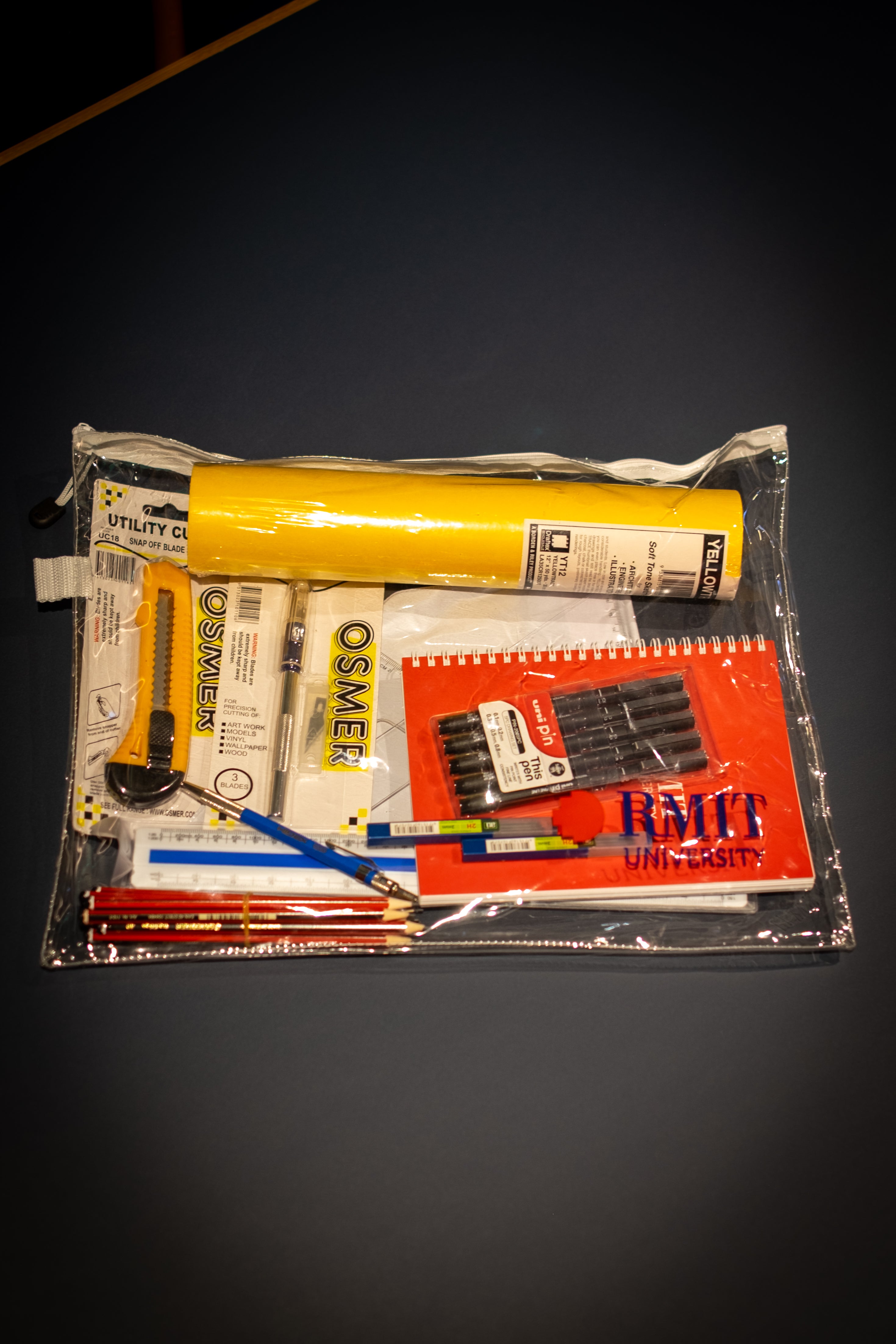 Interior Design and Decoration Kit displayed fully assembled inside a clear zippered storage pouch at RMIT Store, showing Yellowtrace sketch paper roll, red RMIT notebook, black fineliner pens, pencils, mechanical pencil, rulers, utility cutter, precision knife, and assorted drawing tools neatly arranged.