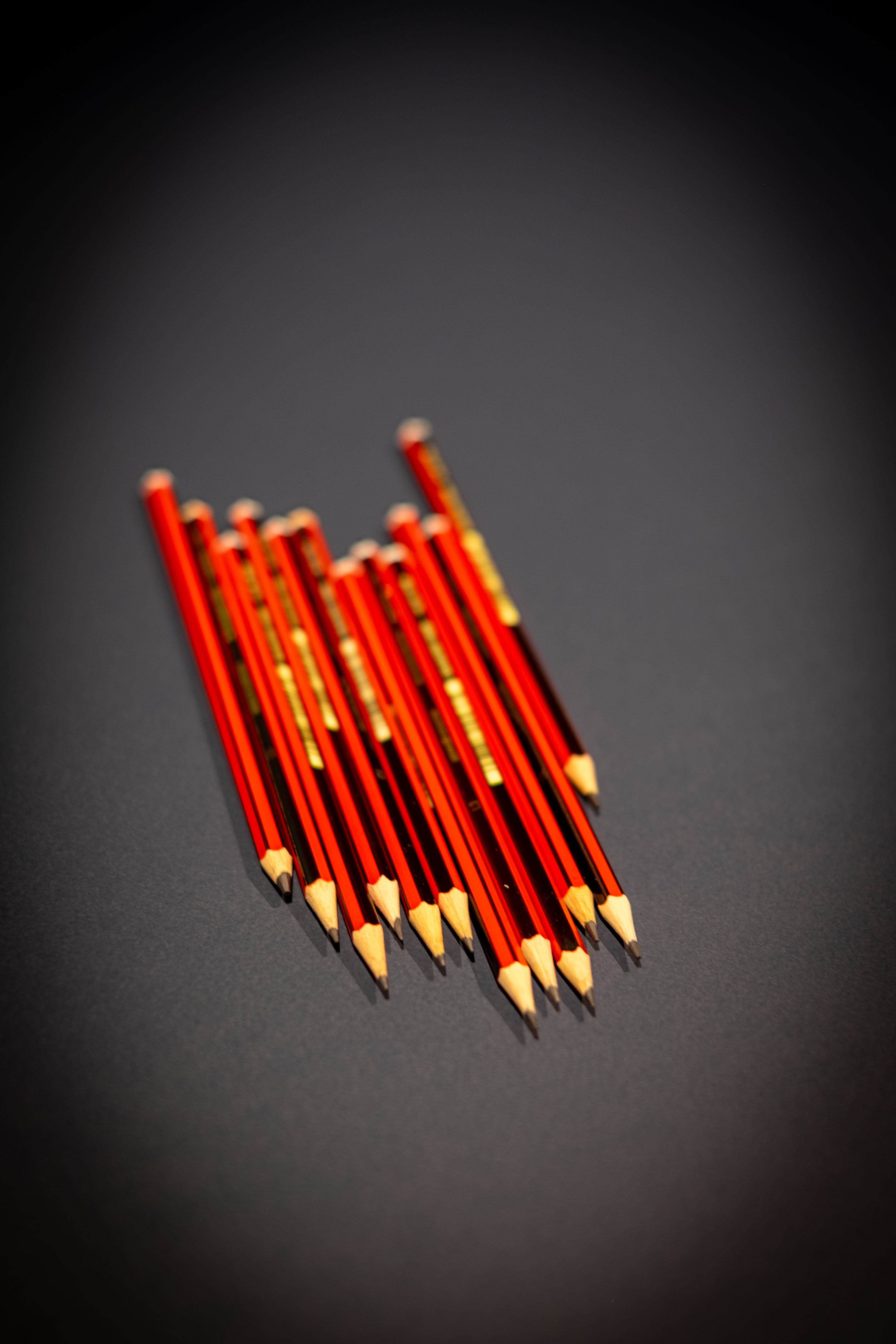Interior Design and Decoration Kit featuring a bundle of sharpened red wooden pencils arranged in a neat stack on a dark tabletop at RMIT Store, showing exposed graphite tips, hexagonal lacquered barrels, gold printed branding, and aligned eraser-free ends.