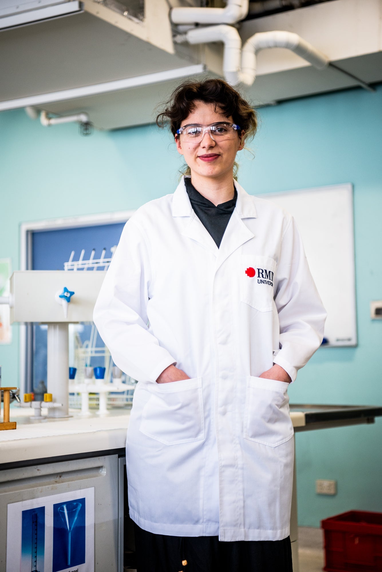 Model wearing a white RMIT University lab coat in a laboratory setting with scientific equipment visible in the background.