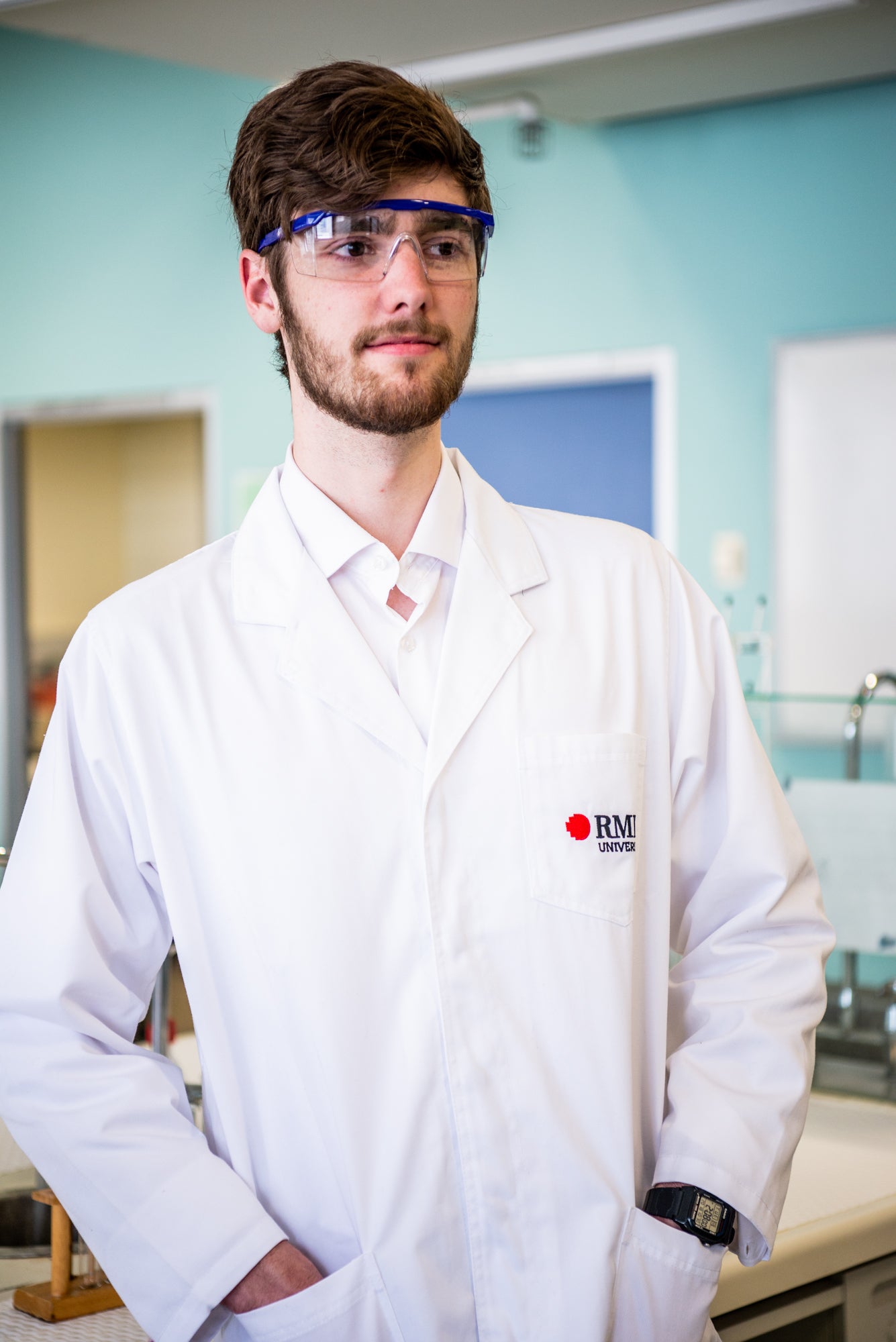 Close-up of a model wearing an RMIT Store lab coat, showcasing the RMIT logo on the chest. The setting includes a laboratory background with visible lab equipment, emphasizing professionalism and practicality.