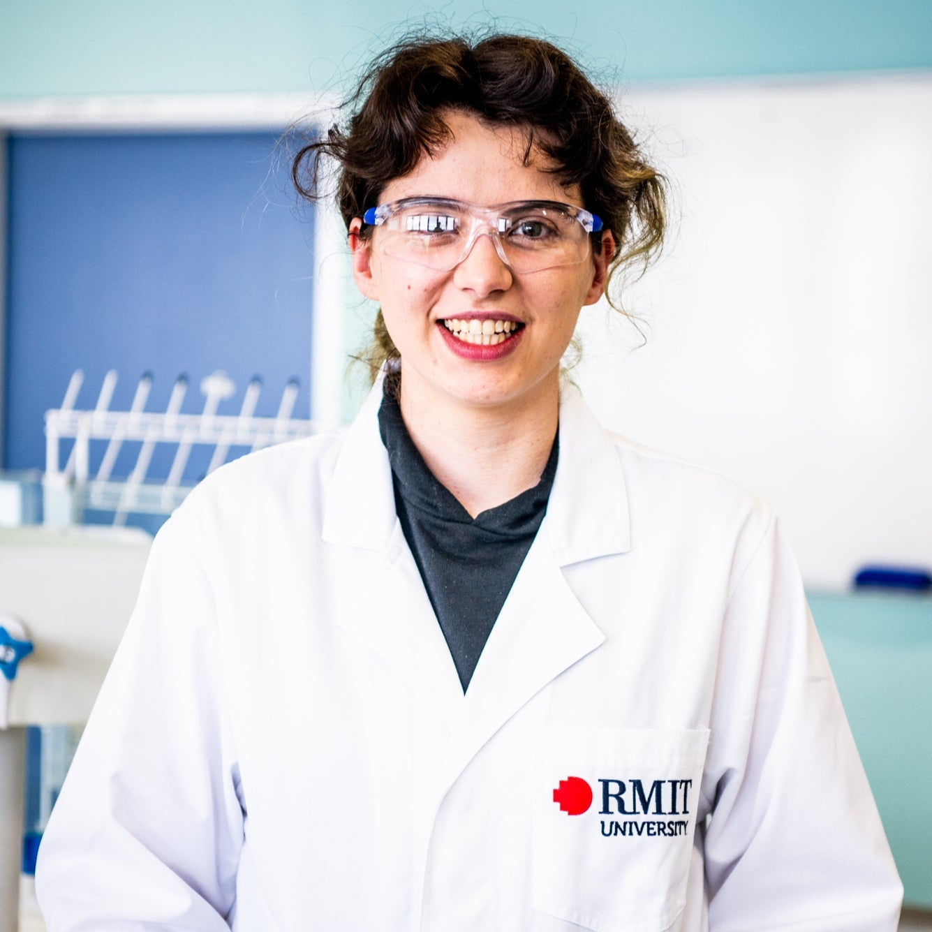 Close-up view of the model wearing the RMIT Store white lab coat in a laboratory, highlighting the front design and RMIT University branded logo.