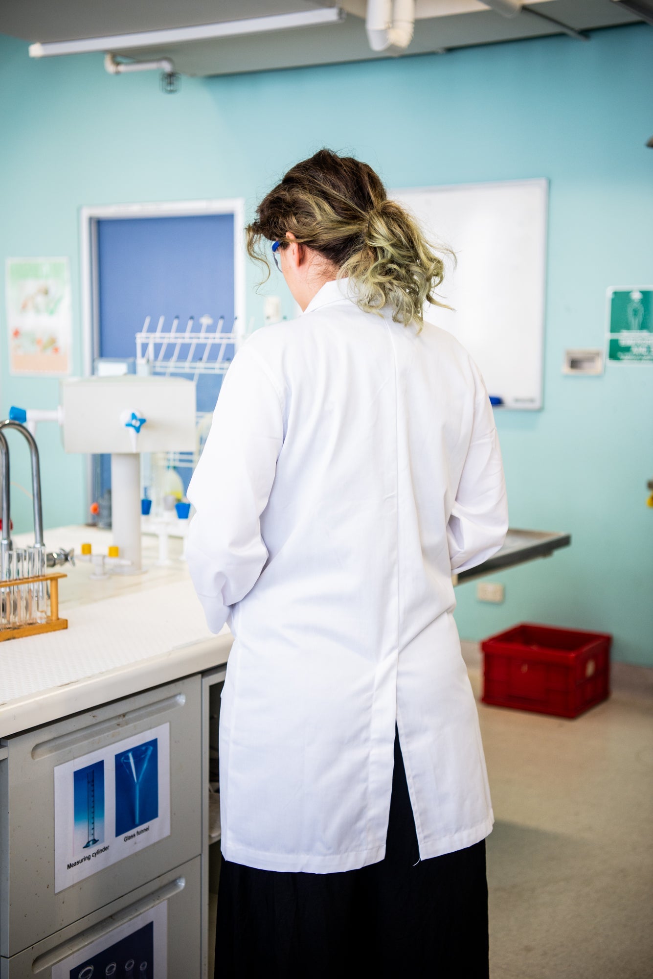 Back view of the RMIT Store white lab coat within a laboratory environment. The coat's full-length coverage provides protection and comfort during scientific work.