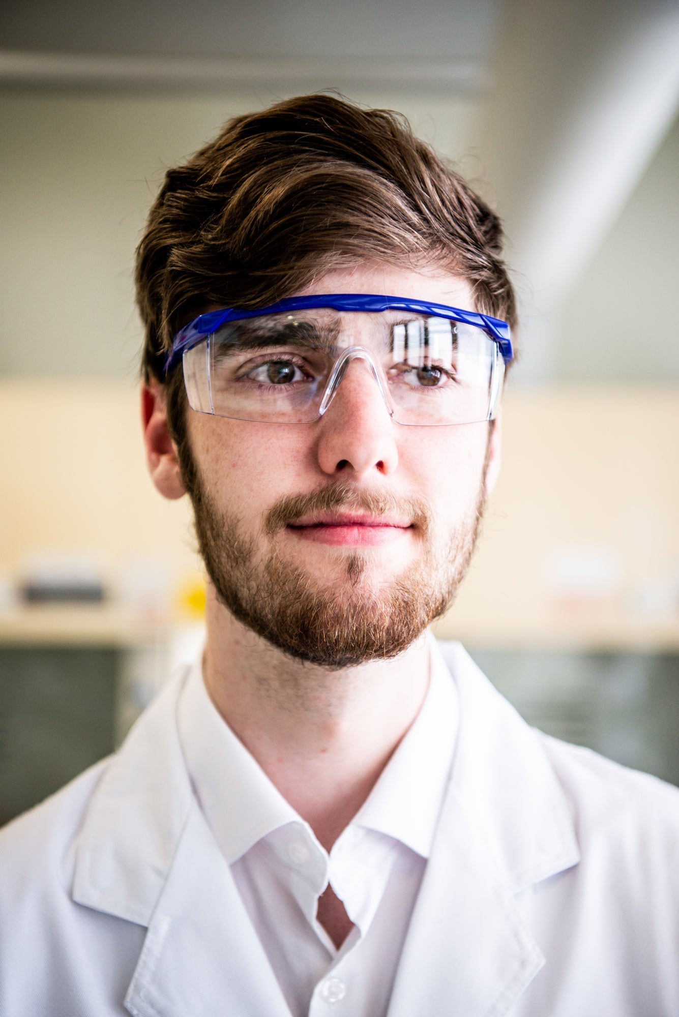 Close-up of a model wearing an RMIT University lab coat and a pair of safety glasses in a lab room.