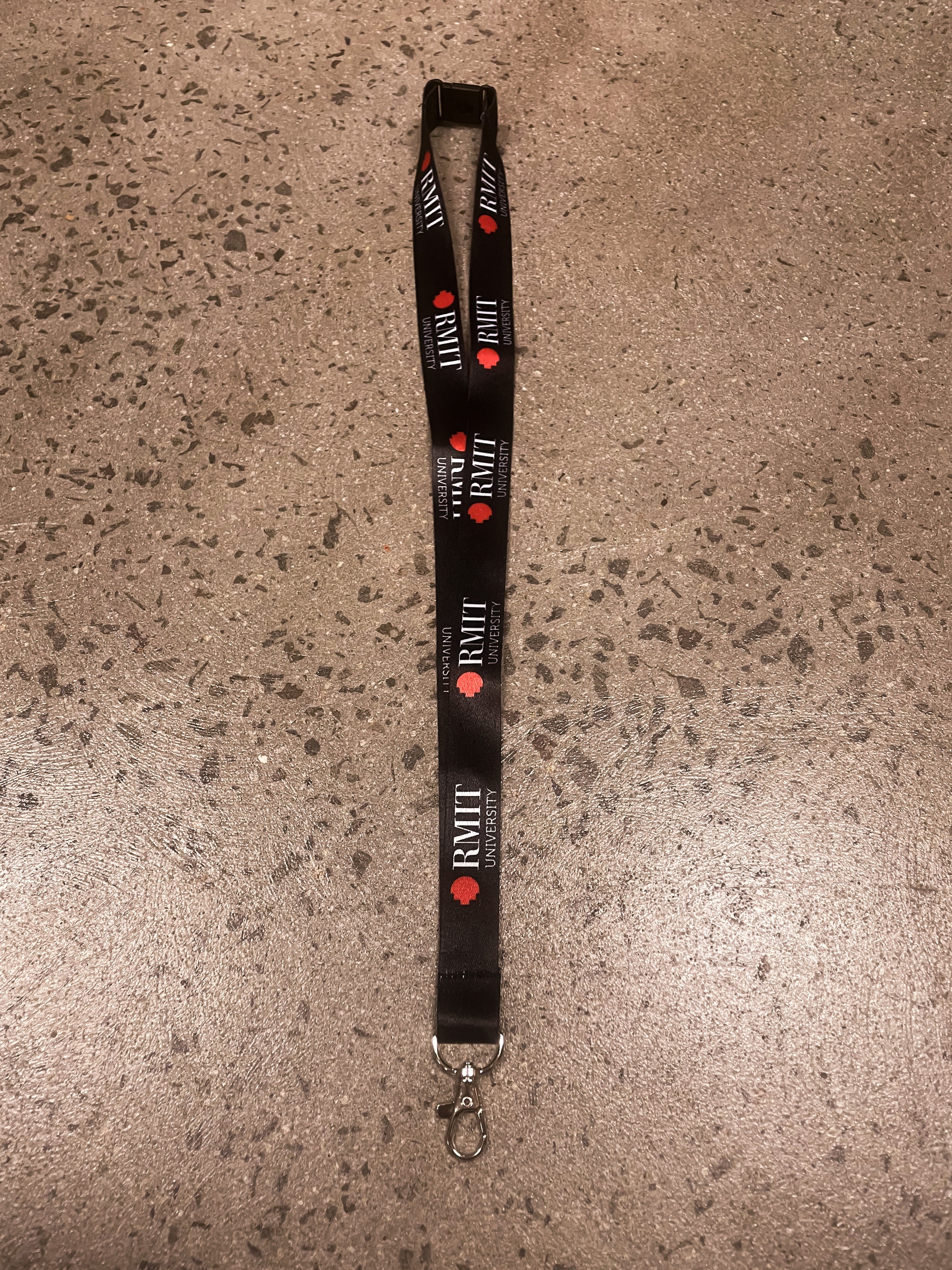 Black RMIT Store lanyard adorned with the RMIT pixel logo in red and RMIT University branding. Laid out flat, featuring a silver clip for convenience and durability.