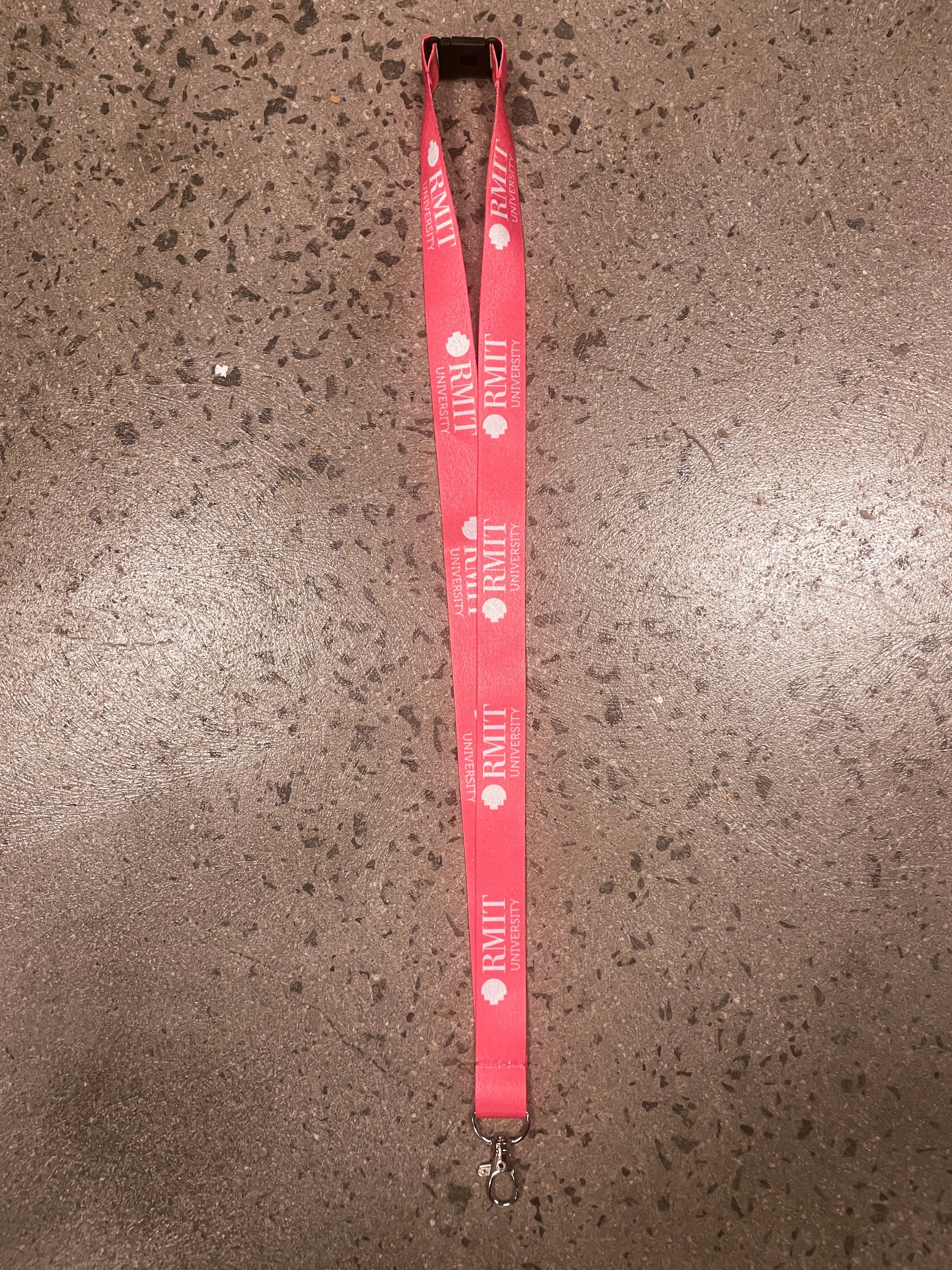 Pink RMIT Store lanyard with the RMIT University logo, displayed flat on a textured surface. Includes a durable silver clip for practical use.