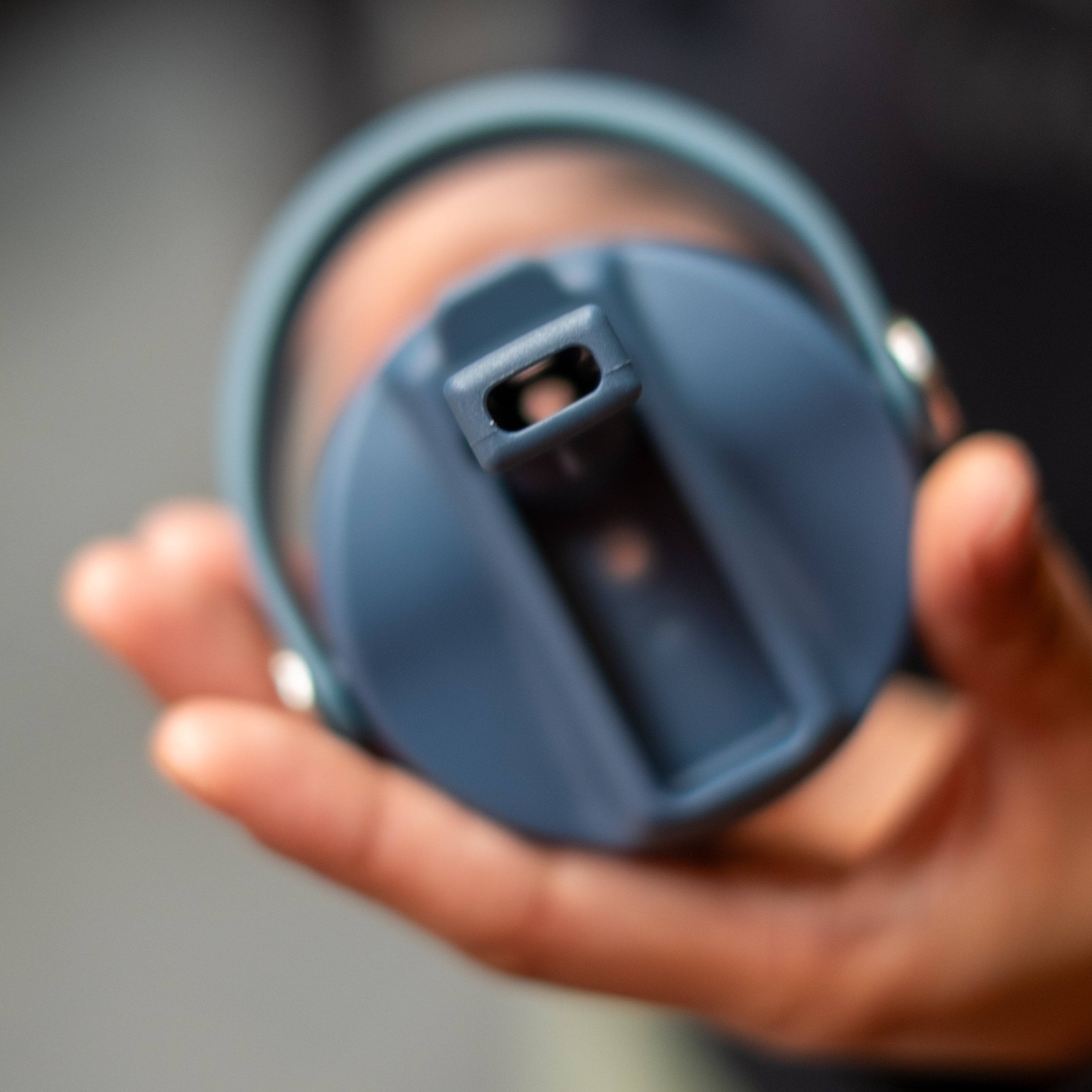 Person holding the lid of an RMIT Store Limited Edition Drink Bottle in Petrol Blue, featuring a flip valve spout and visible mouthpiece of the integrated straw. The lid includes a sturdy, movable handle designed for easy carrying and a secure fit
