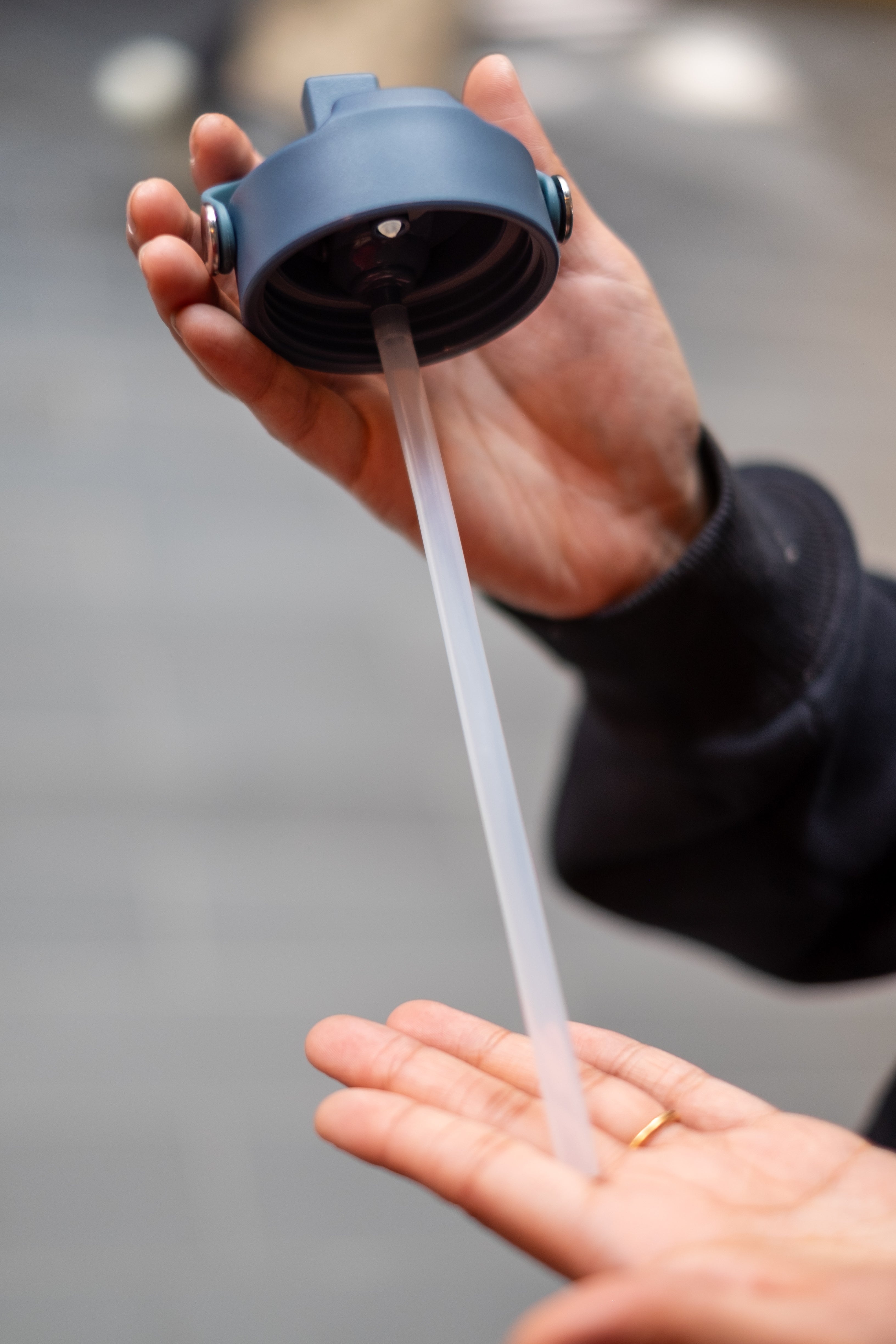 Person holding the lid of an RMIT Store Limited Edition Bottle in Petrol Blue, showcasing the integrated straw mechanism. The lid features a sturdy, movable handle for easy carrying and a secure screw-on design for leak-proof functionality.