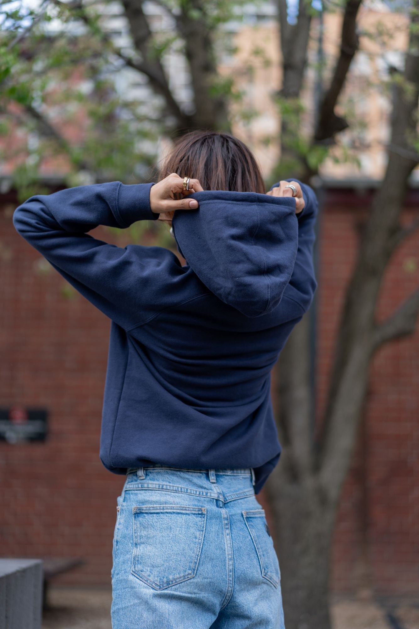 A model wearing the RMIT Ltd Ed Hoodie in midnight blue, displaying the back view with the hood being adjusted. The hoodie is crafted from soft, durable material, ideal for comfort and style. Available at the RMIT Store.