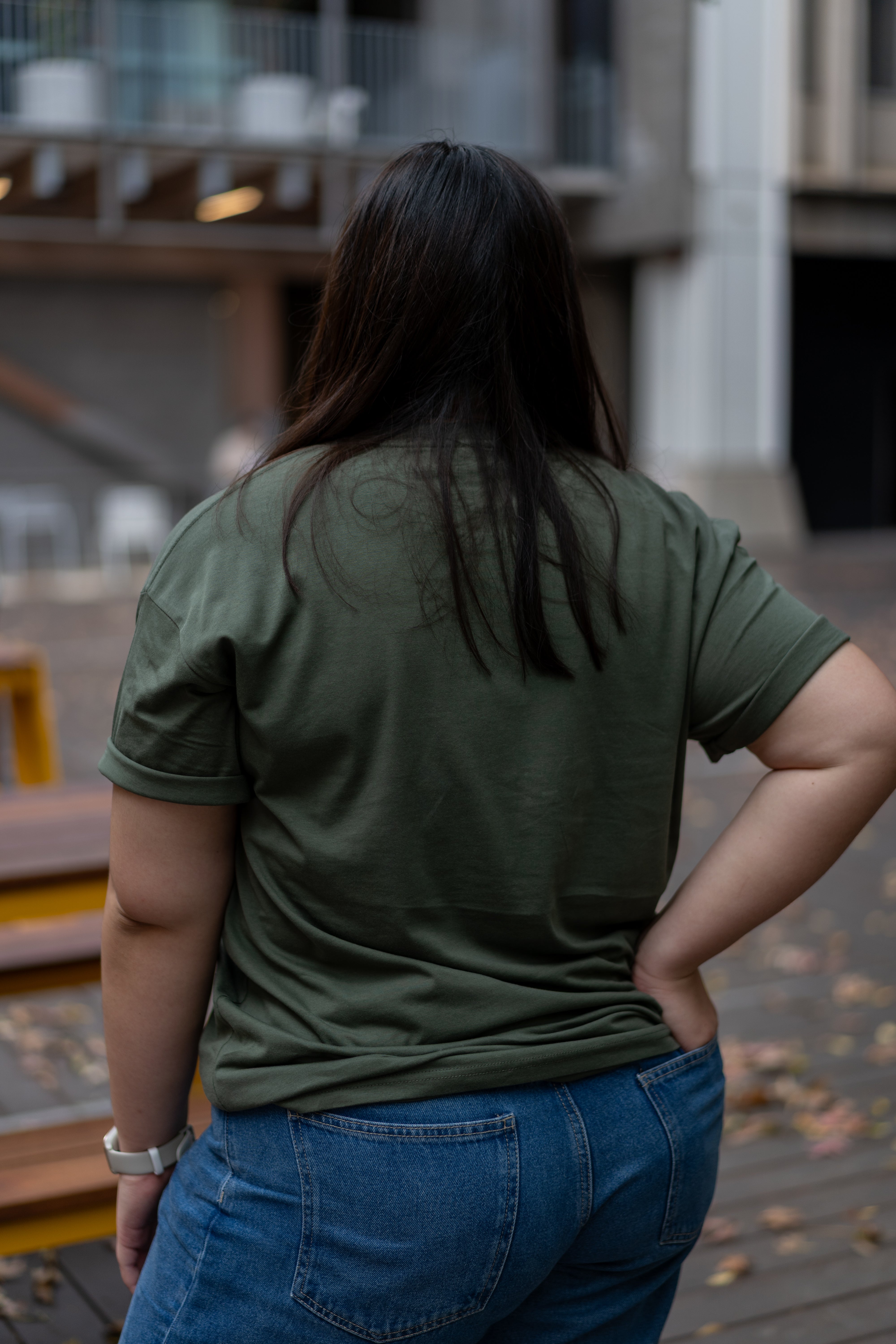 Rear view of model wearing the RMIT Ltd Ed Tee in Cypress green, showing the simplicity of the tee's back design. Styled casually with blue jeans, available at the RMIT Store.