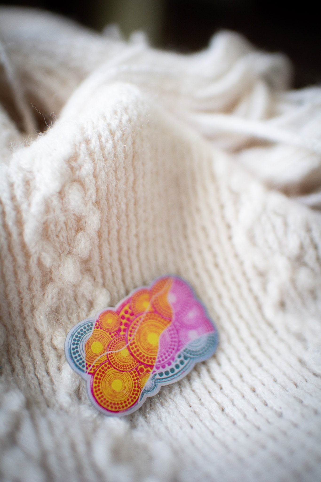 Angled view of the pink Luwaytini pin resting on a white knit sweater, showing the pin's vibrant colour and curved design detail against the textured fabric, available at the RMIT Store.
