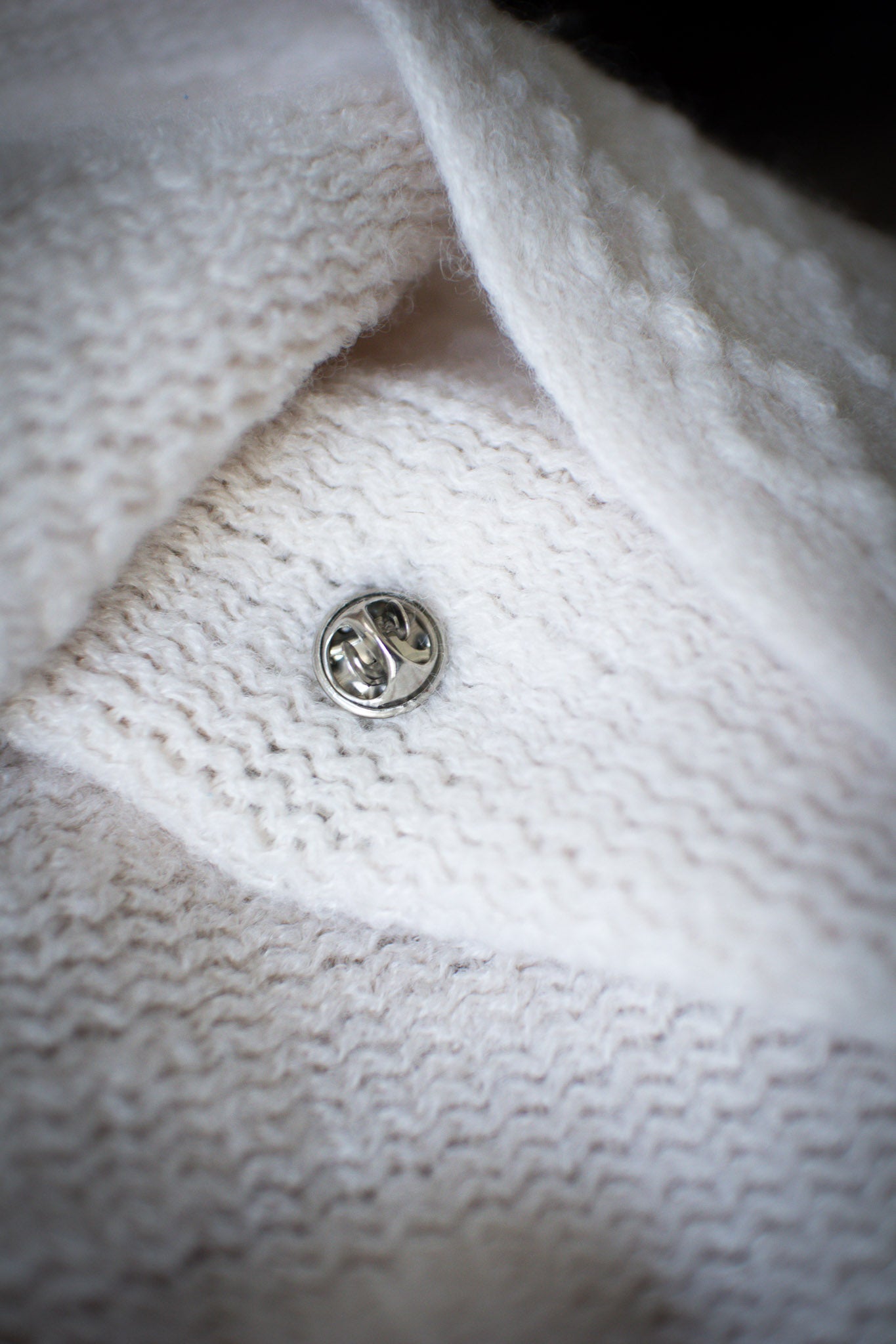 Back view of Luwaytini pin showing metal pin clasp, pinned securely on a white knit sweater with textured fabric visible, available at the RMIT Store.