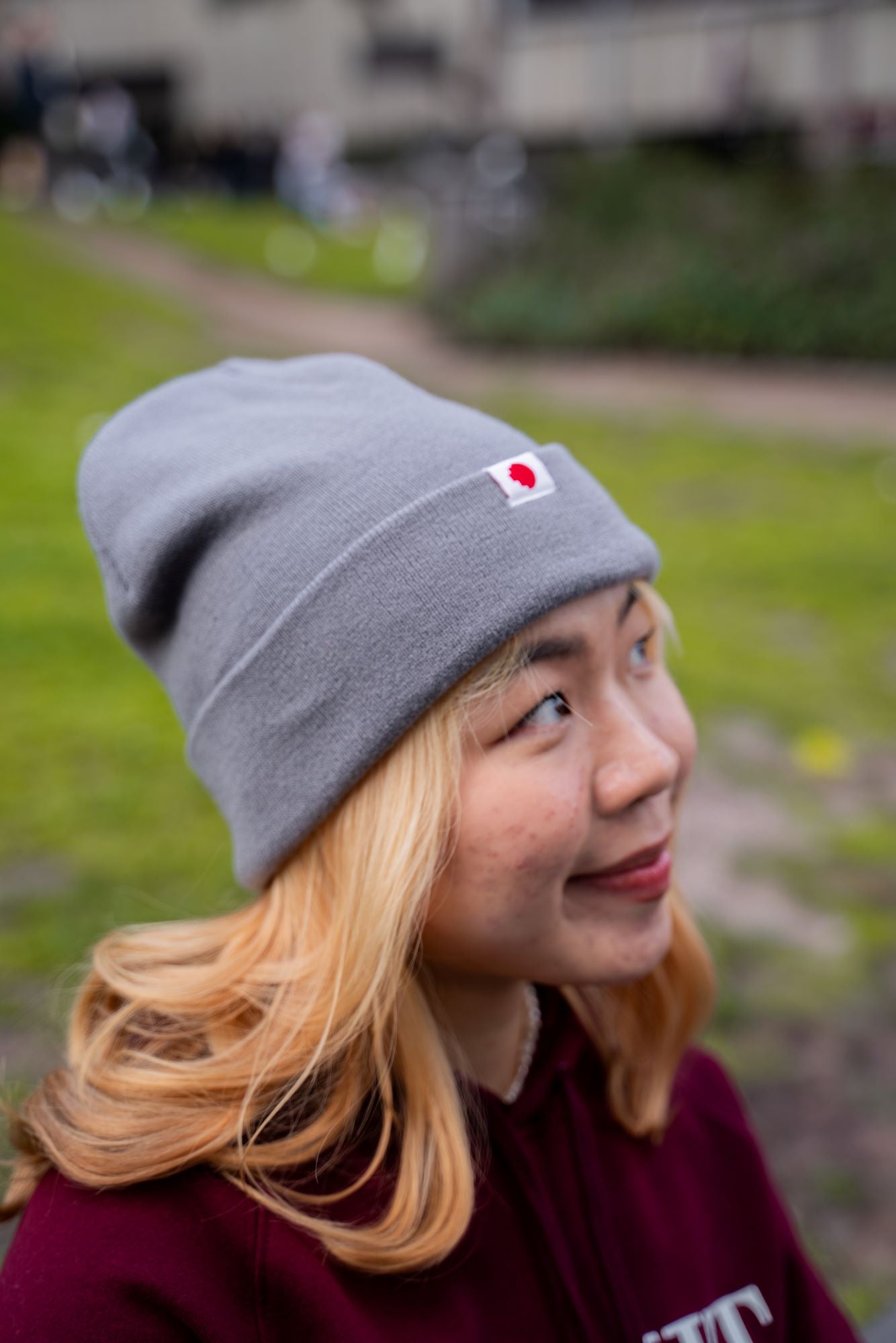 Close-up side view of a female model wearing the RMIT Luxe Beanie in grey, showing the ribbed knit texture and folded cuff with a small woven RMIT logo tag on the front.
