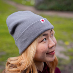 Close-up side view of a female model wearing the RMIT Luxe Beanie in grey, showing the ribbed knit texture and folded cuff with a small woven RMIT logo tag on the front.