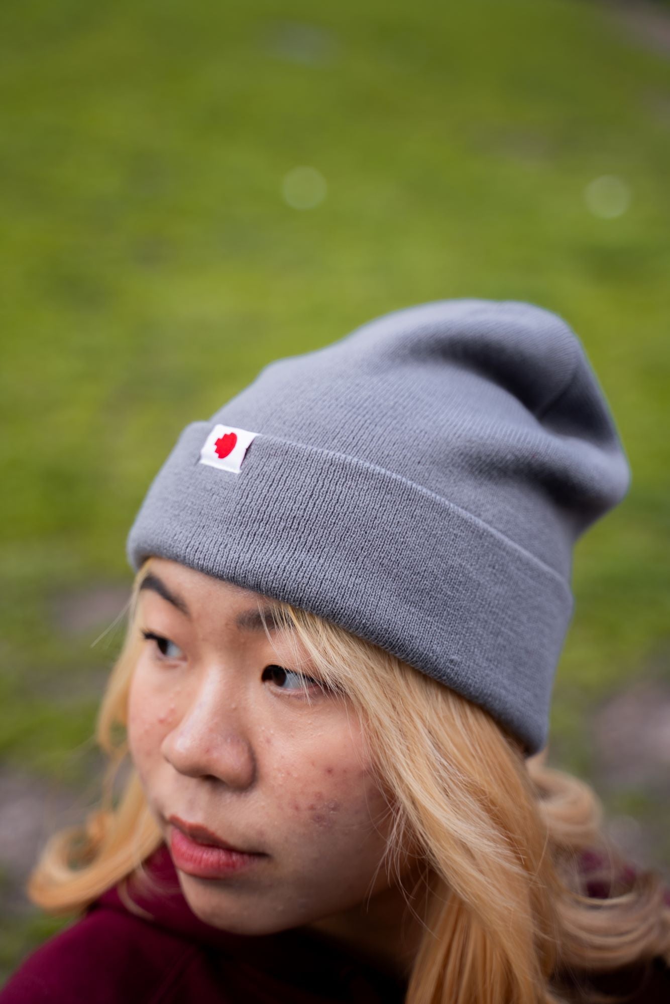 Close-up of a female model wearing the RMIT Luxe Beanie in grey, showing the ribbed knit texture and folded cuff with a small woven RMIT logo tag on the front. 