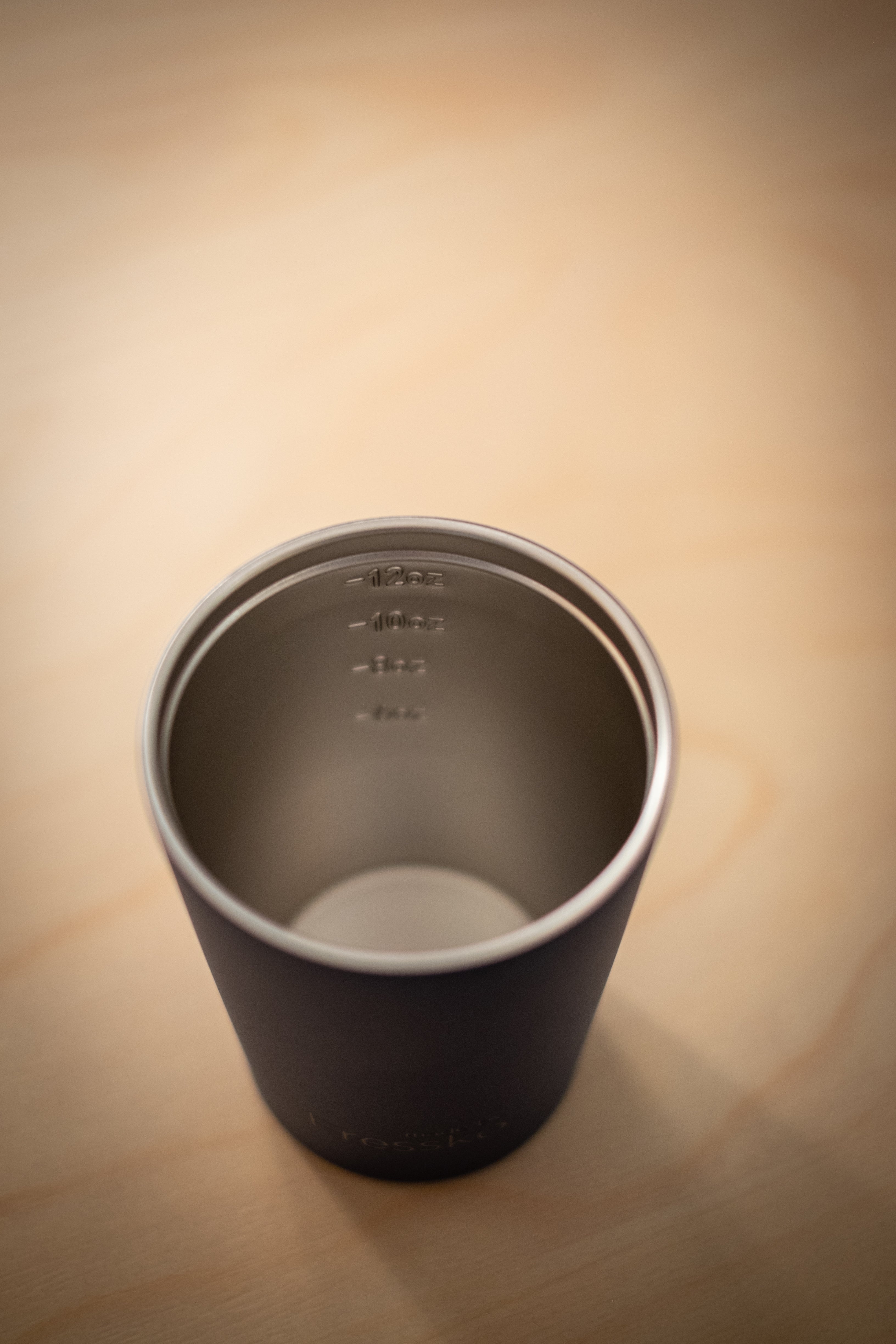 Made by Fressko x RMIT Reusable Cup in matte black viewed from above with lid removed at RMIT Store, revealing stainless steel interior with engraved measurement markings for 12oz, 10oz, 8oz, and 4oz, smooth reflective lining, and rounded base.