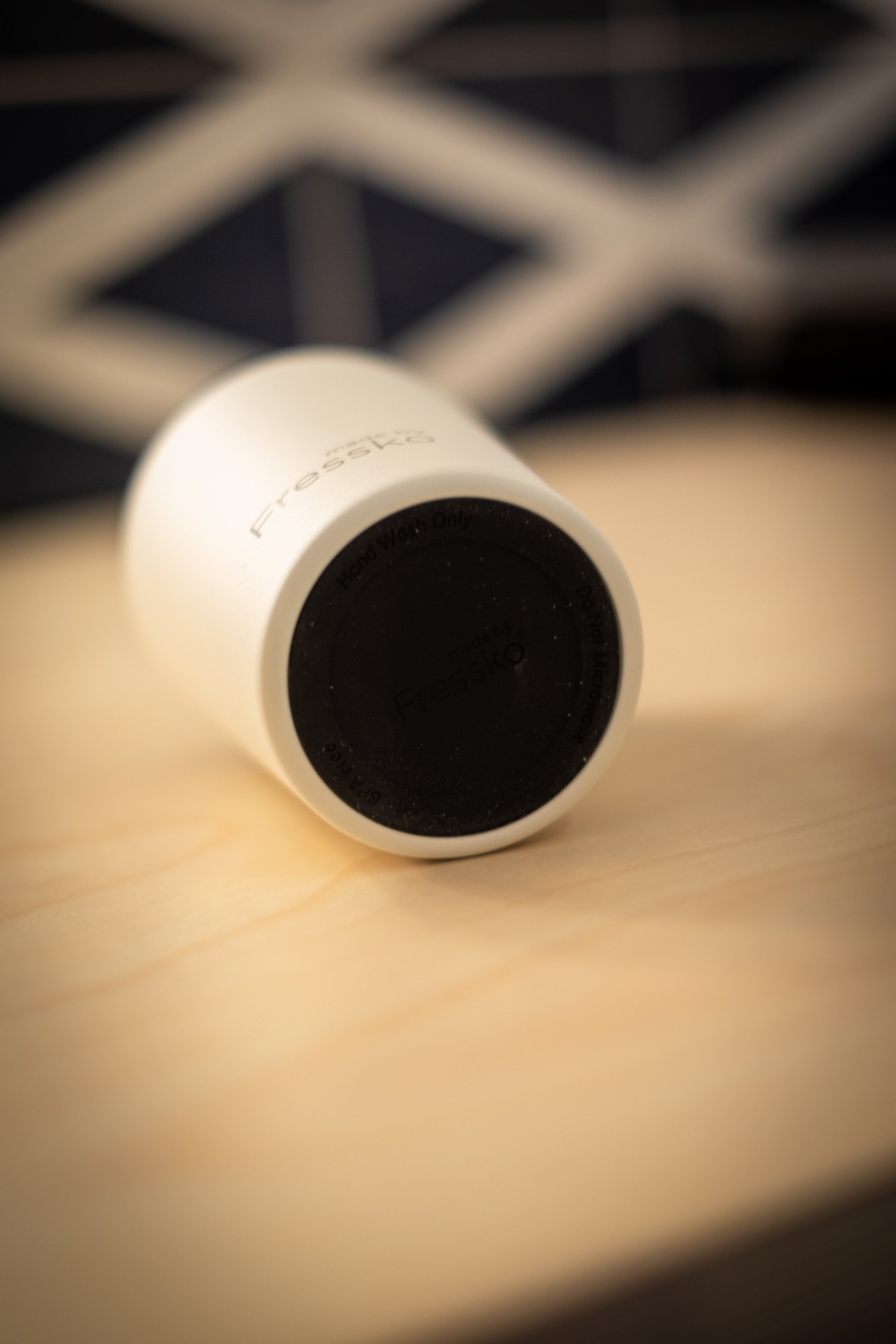 Made by Fressko x RMIT Reusable Cup in matte white lying horizontally on a wooden surface at RMIT Store, showing subtle grey “Fressko” branding near the base and embossed black rubber underside.