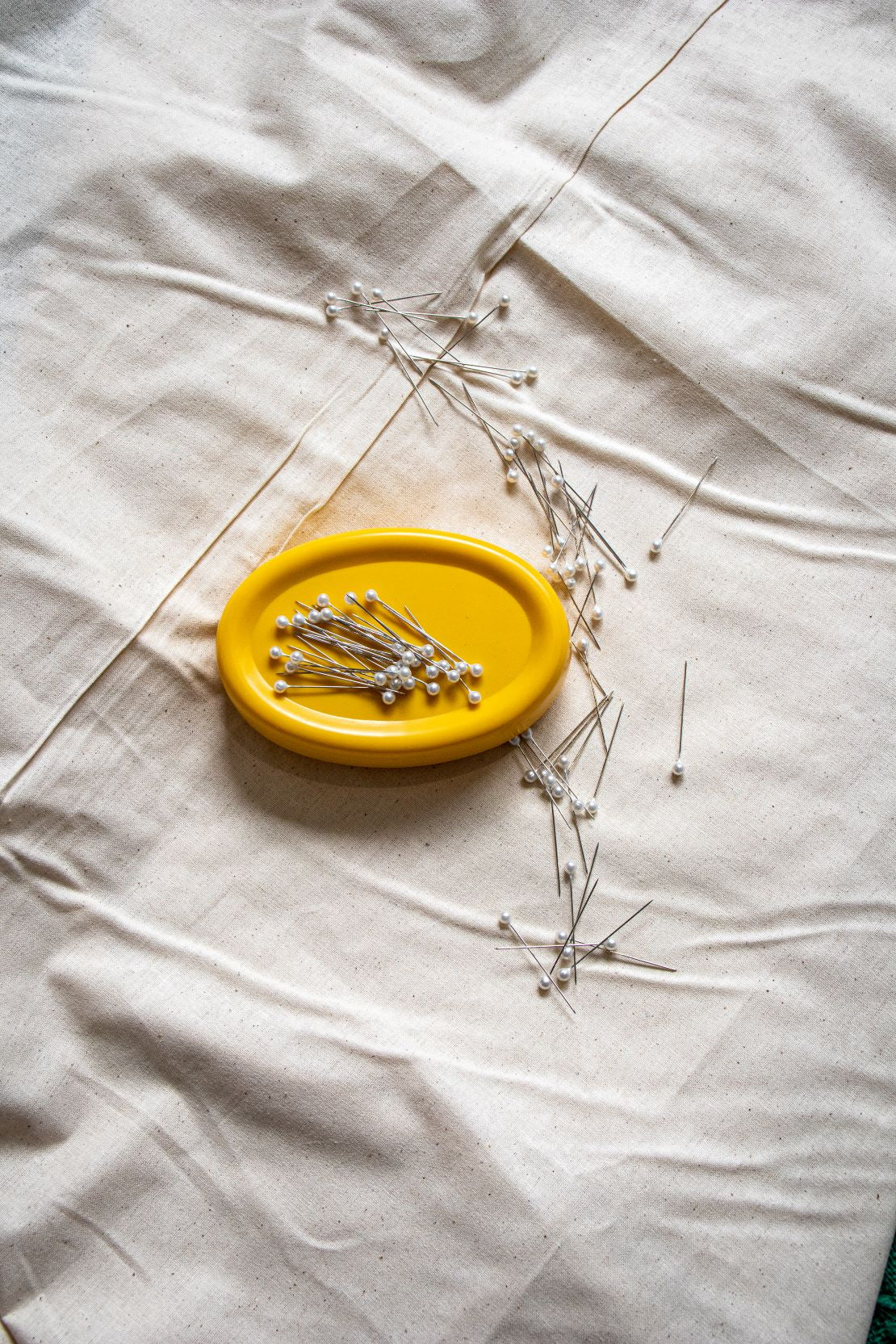 Top view of the yellow magnetic pin holder from the RMIT Store, with several pearl-headed pins scattered across the surface and some resting on the beige fabric underneath. Available from the RMIT Store.