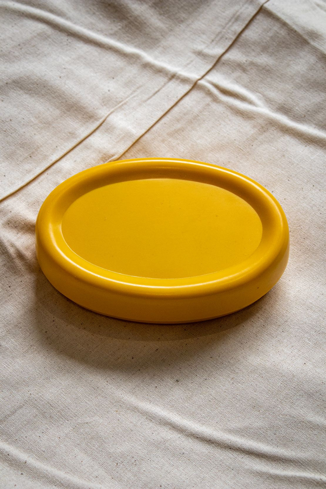 Rear view of the yellow oval magnetic pin holder showing its smooth base and curved shape, placed on a beige fabric tabletop, available from the RMIT Store.