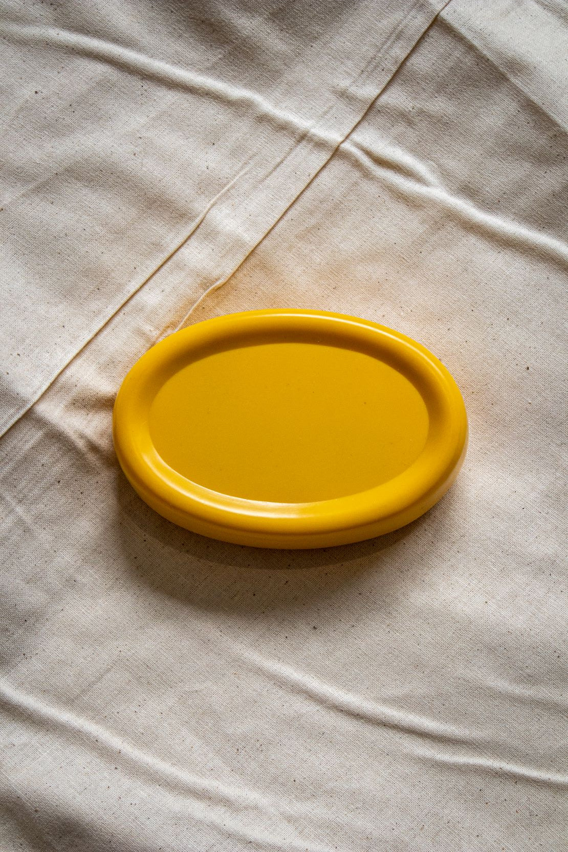 Rear view of the yellow oval magnetic pin holder showing its smooth base and curved shape, placed on a beige fabric tabletop, part of the RMIT Store sewing tools collection.