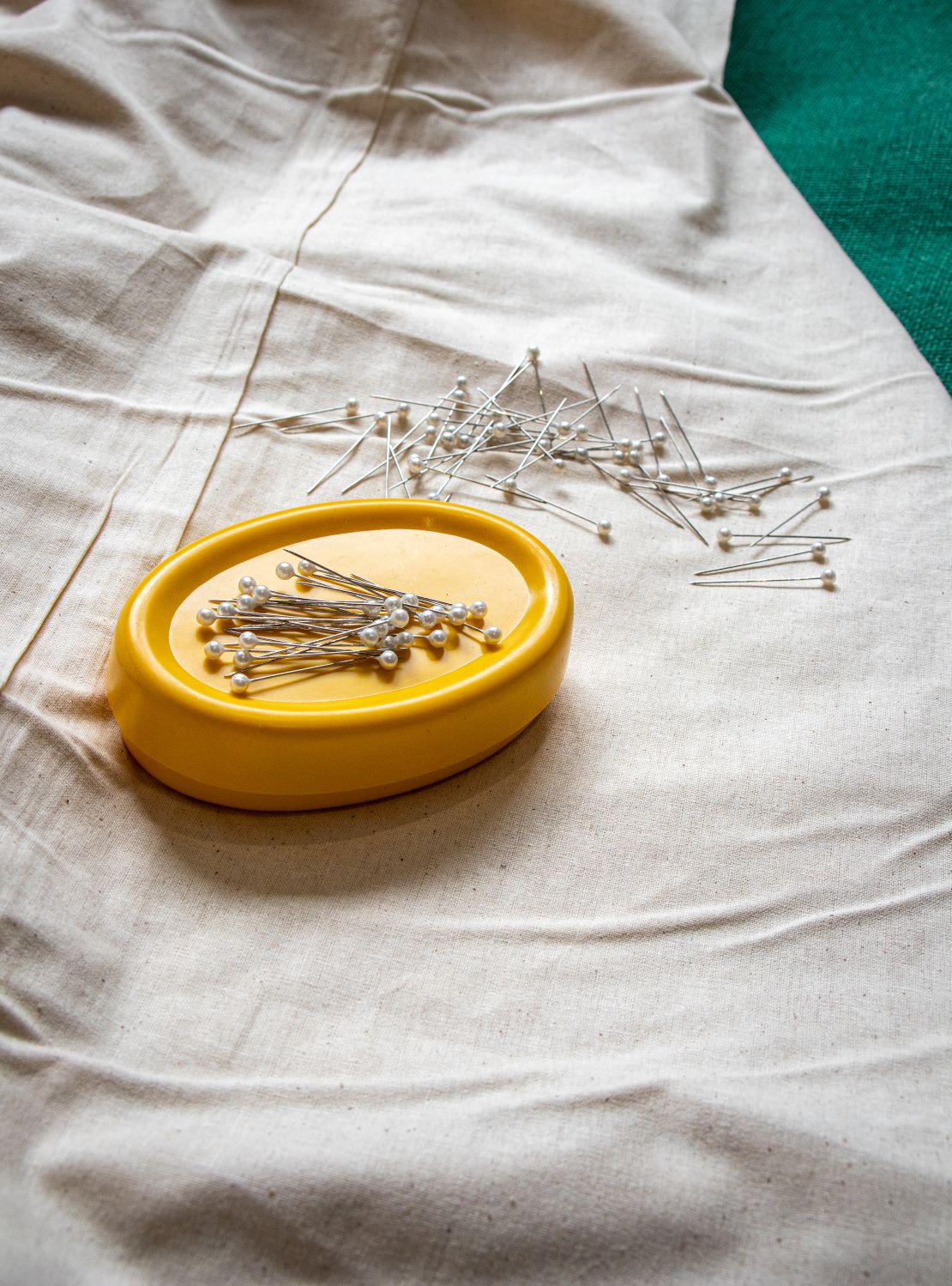 Yellow oval-shaped magnetic pin holder with assorted pearl-headed pins scattered loosely on the surface, displayed on a beige fabric tabletop, available from the RMIT Store.