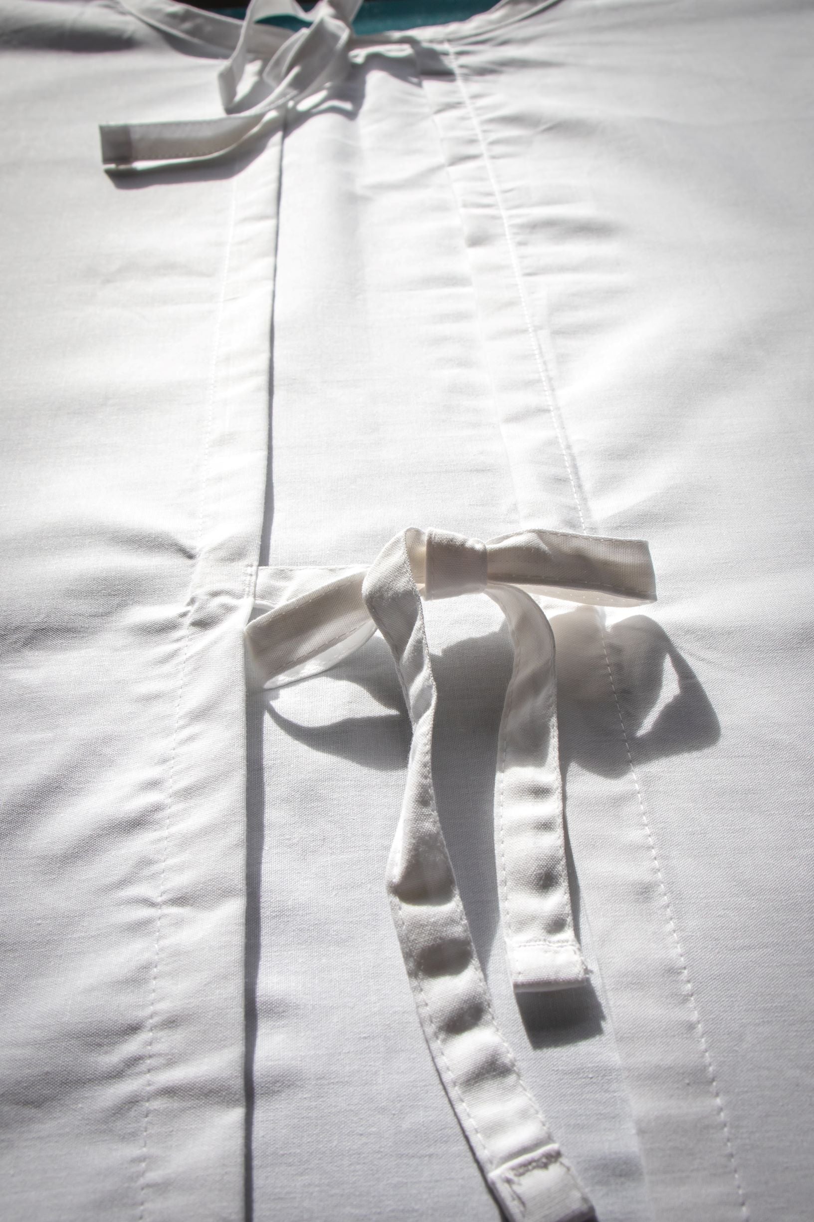 Close-up view of the two fabric ties at the back of the white Medical Lab Gown from the RMIT Store. One tie is near the neck area, and the other is positioned just below it. The ties are used to secure the gown, highlighting its functional design. The background is neutral, focusing on the ties' placement and the gown’s simplicity.