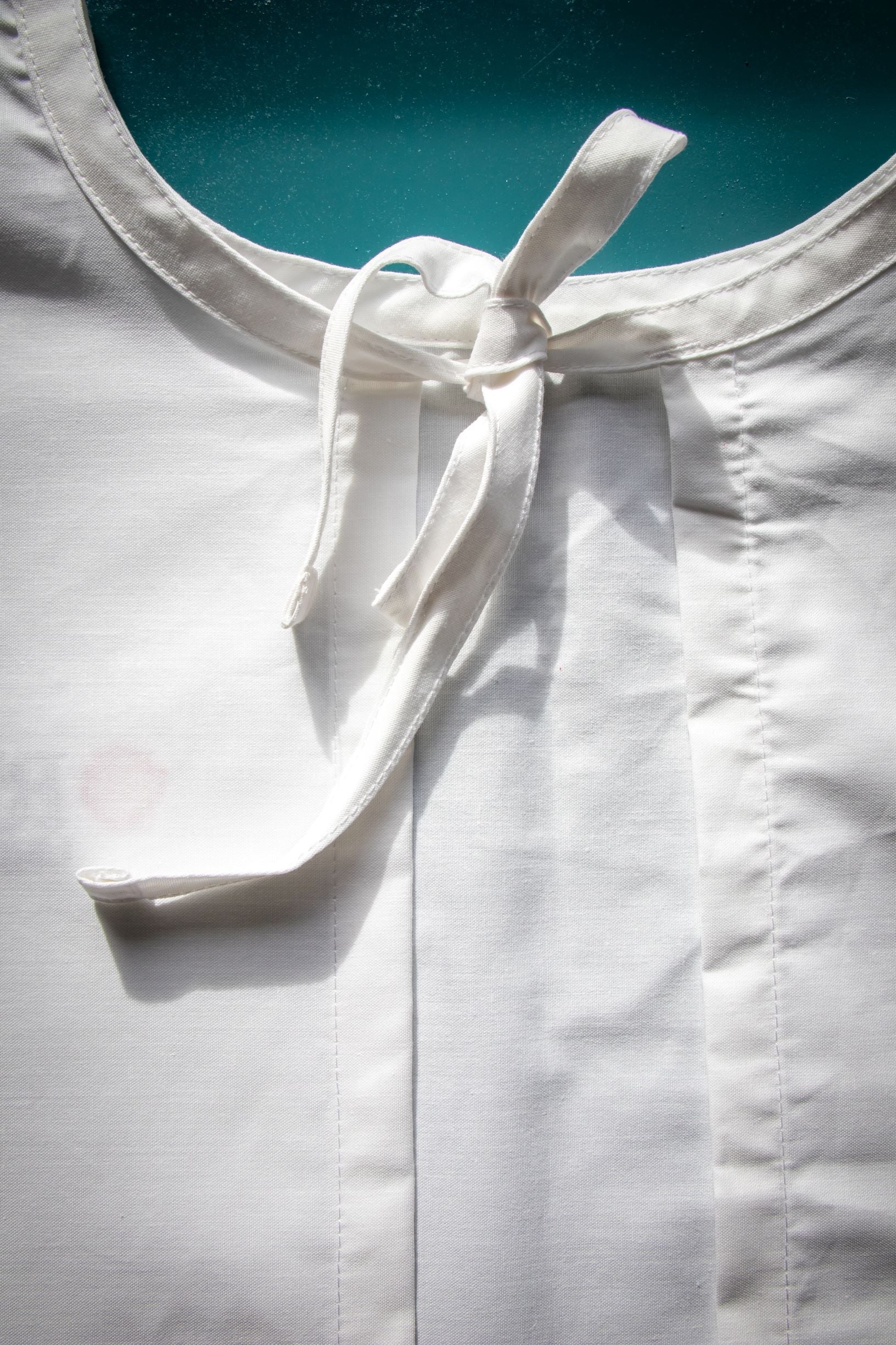 Close-up rear view of the white Medical Lab Gown from the RMIT Store, showing a single white fabric tie fastened near the round neckline. The gown is laid flat.