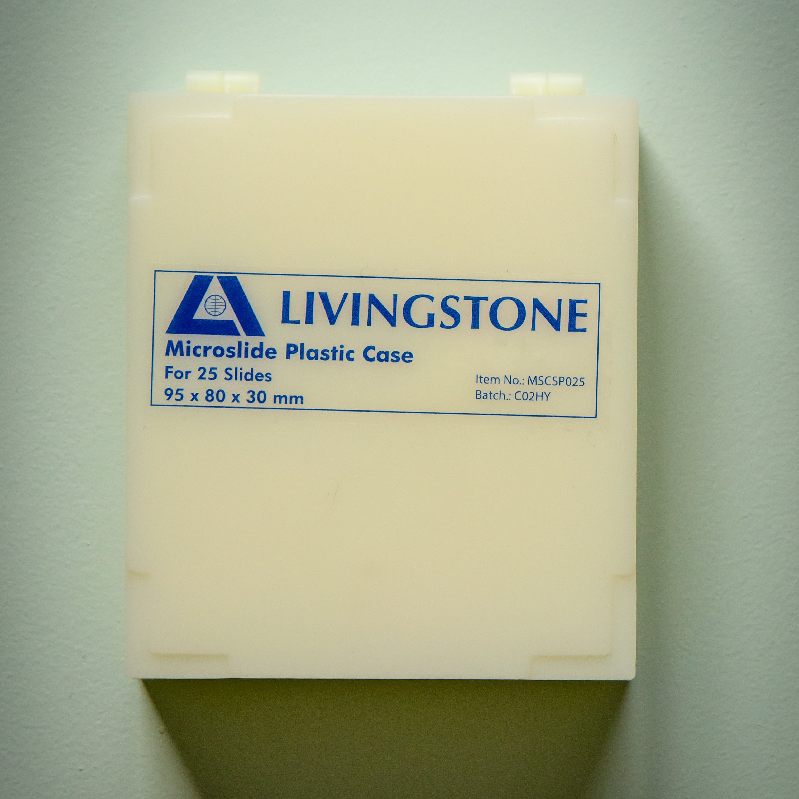 Microslide Plastic Case by Livingstone, closed front view in off-white reusable plastic with a blue printed LIVINGSTONE logo, Microslide Plastic Case branding, capacity for 25 slides, dimensions 95 × 80 × 30 mm, item number MSCSP025 and batch code C02HY visible on the front label. The hinged slide storage case is photographed against a plain light background for the RMIT Store product catalogue.