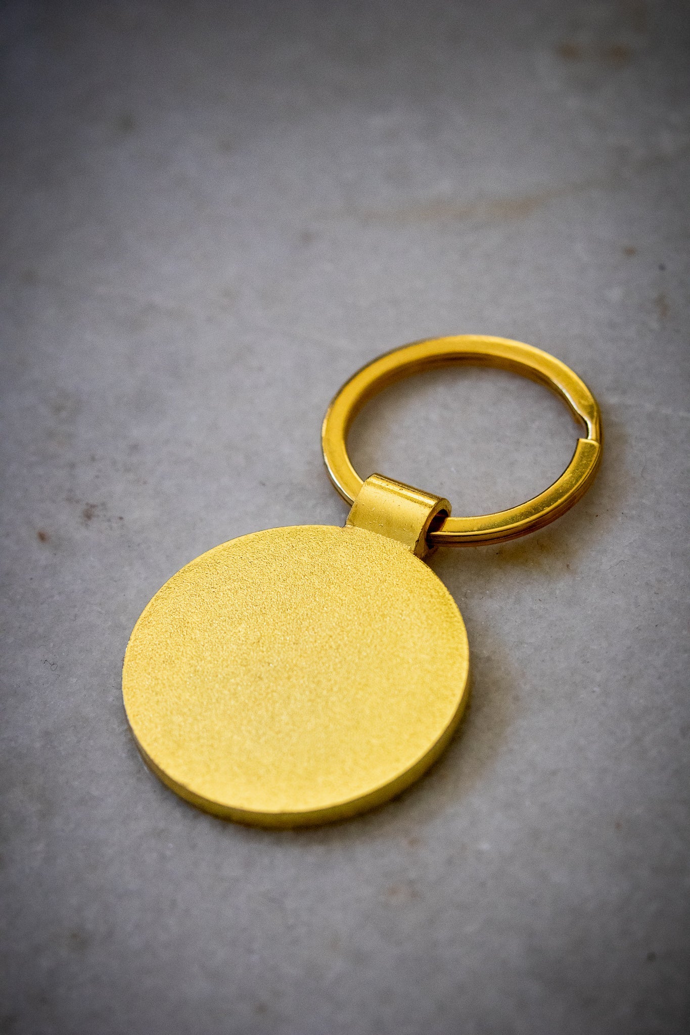 Back view of the RMIT motto lapel keyring showing gold enamel finish, set against a light background, available at the RMIT Store.