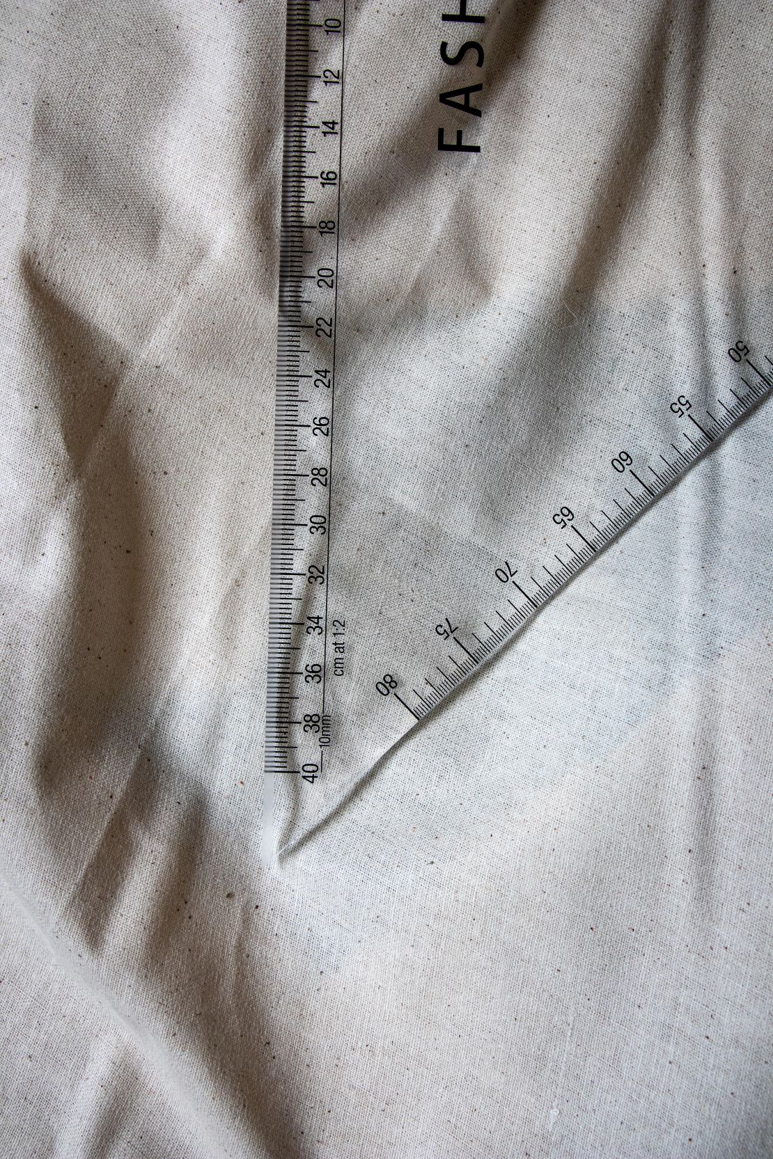 Close-up vertical view of the Multi Scale Ruler DM4 from the RMIT Store, showing precise black measurement markings on clear plastic with a beige fabric background.