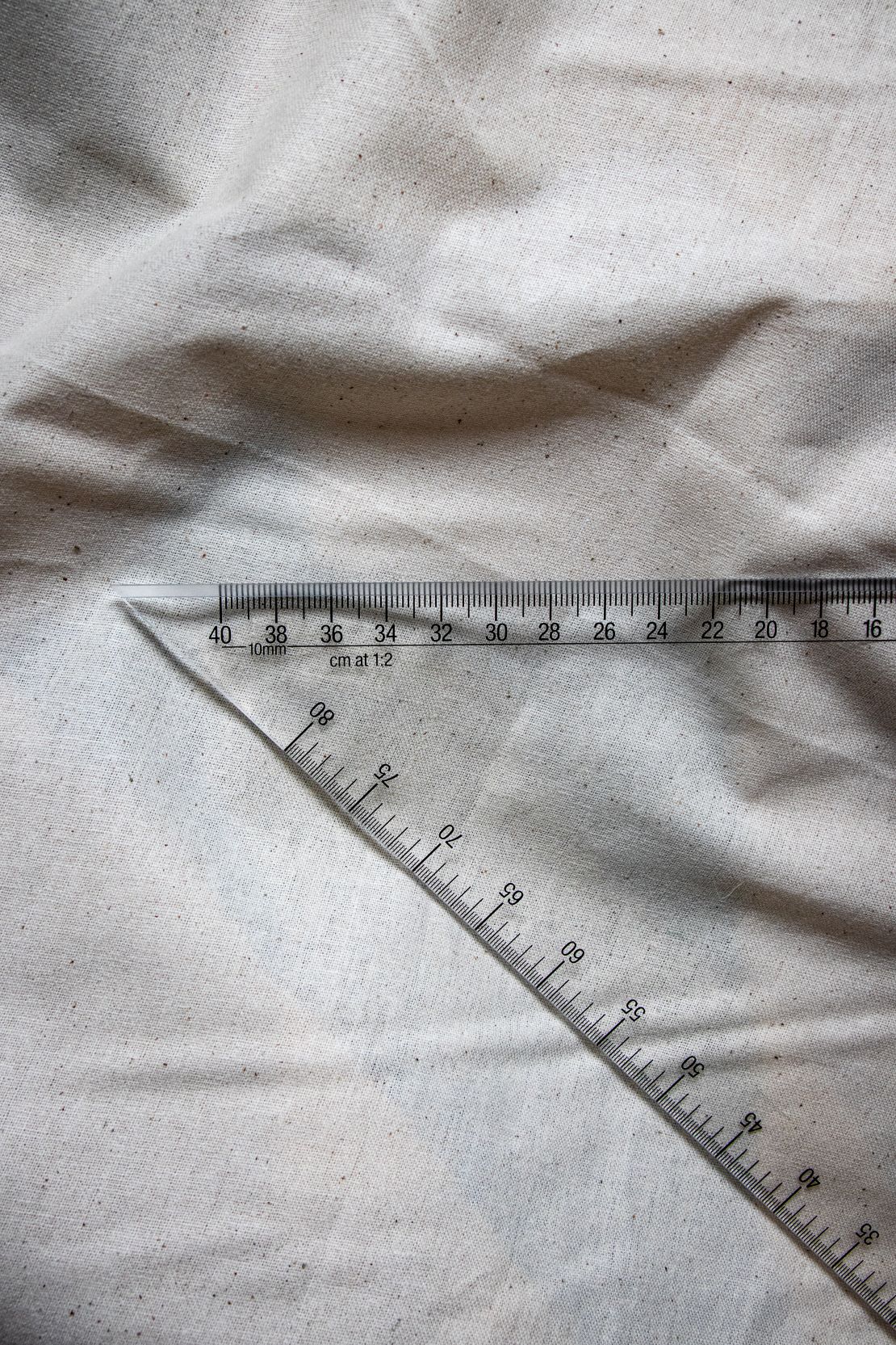 Close-up angled view of the Multi Scale Ruler DM4 from the RMIT Store, showing clear plastic construction with black measurement markings and a scale from 0 to 10 cm, placed on a beige fabric surface.