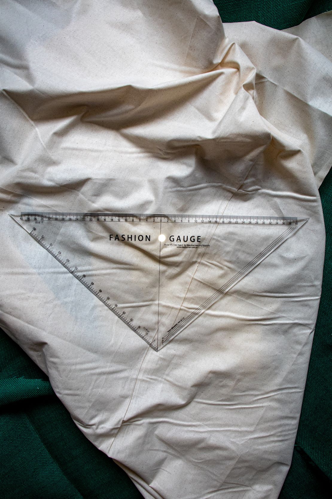 Top-down horizontal view of the Multi Scale Ruler DM4 from the RMIT Store, displaying full length of clear plastic ruler with black measurement scales, lying flat on beige fabric.