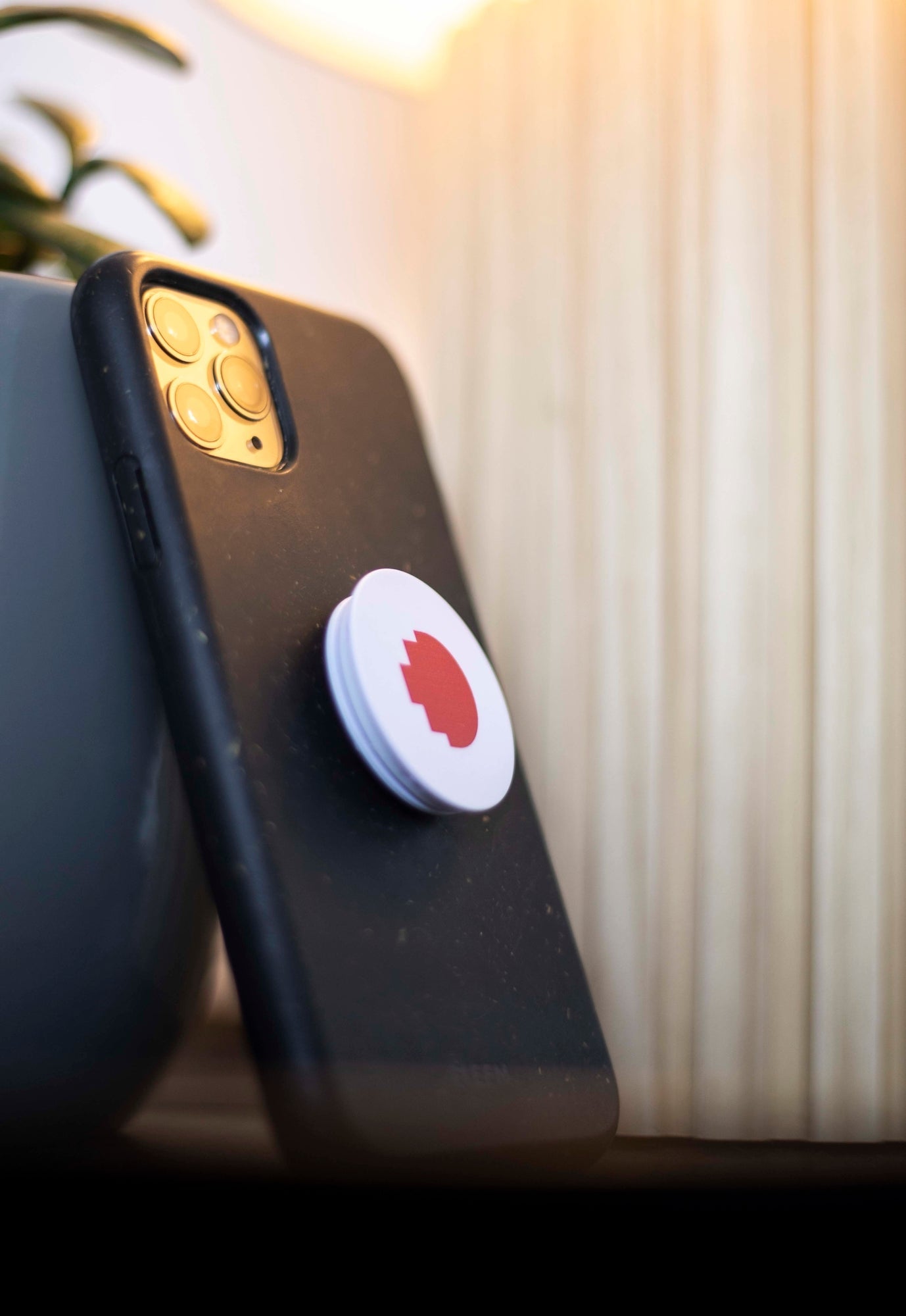 Close-up front view of the RMIT Store Phone Grip featuring the RMIT pixel logo in red shades on a white circular base, attached to the back of a black smartphone.