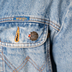 Model wearing the RMIT Pixel Lapel Pin on a blue denim jacket pocket. The pin features the RMIT logo with a red and grey design, highlighting brand loyalty from the RMIT Store.