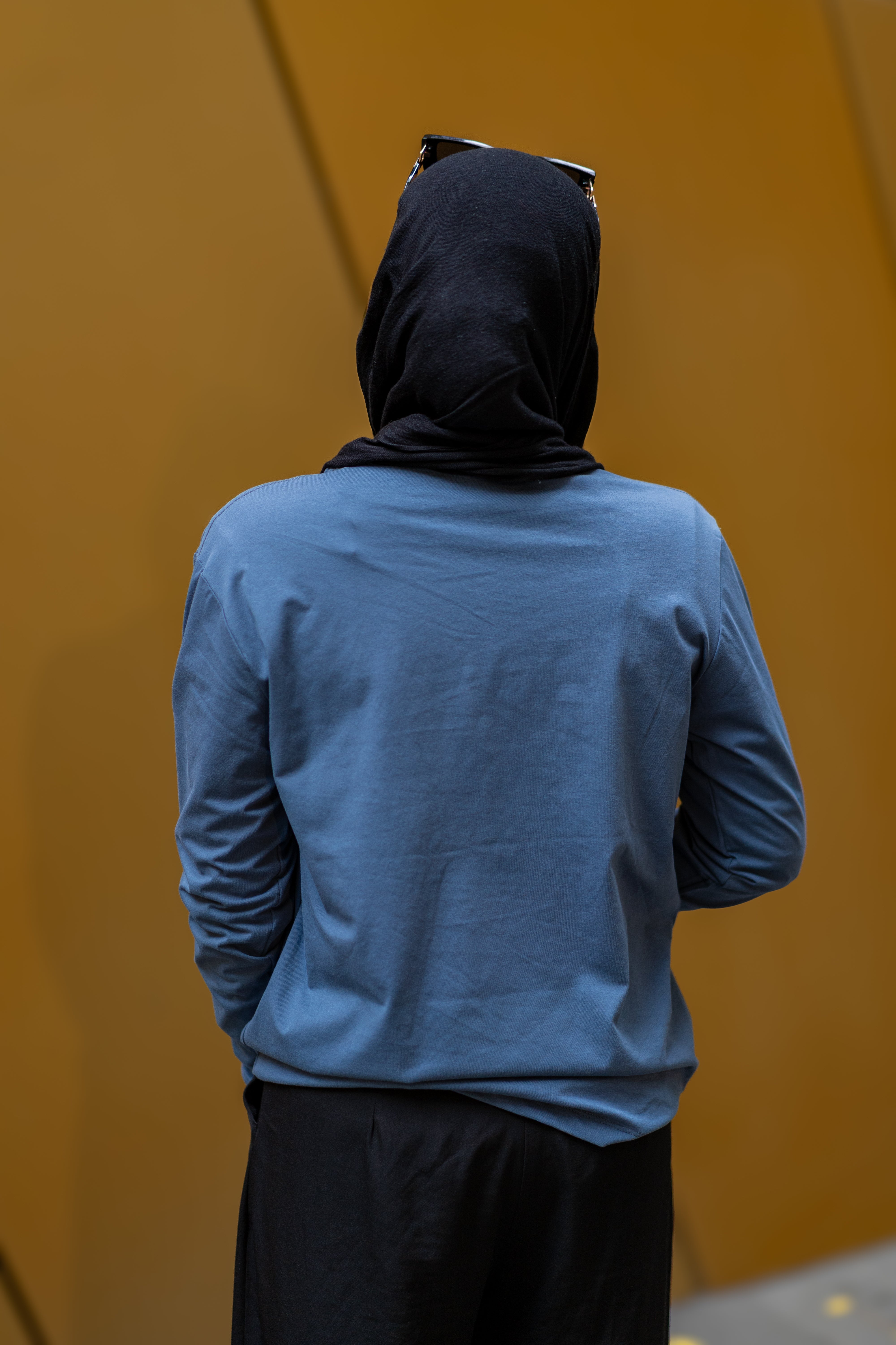 Back view of a female model wearing RMIT Plent Long Sleeve Tee in slate blue with black trousers, showcasing the tee's casual fit and drape.