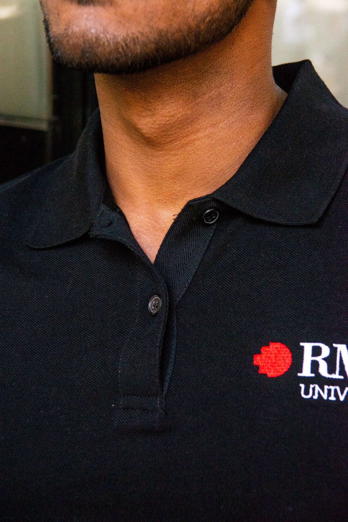 Close-up of the model wearing the black RMIT Polo, focusing on the collar and buttons. The RMIT University logo stands out, underscoring the polo's quality and uniform appeal, marketed by the RMIT Store.
