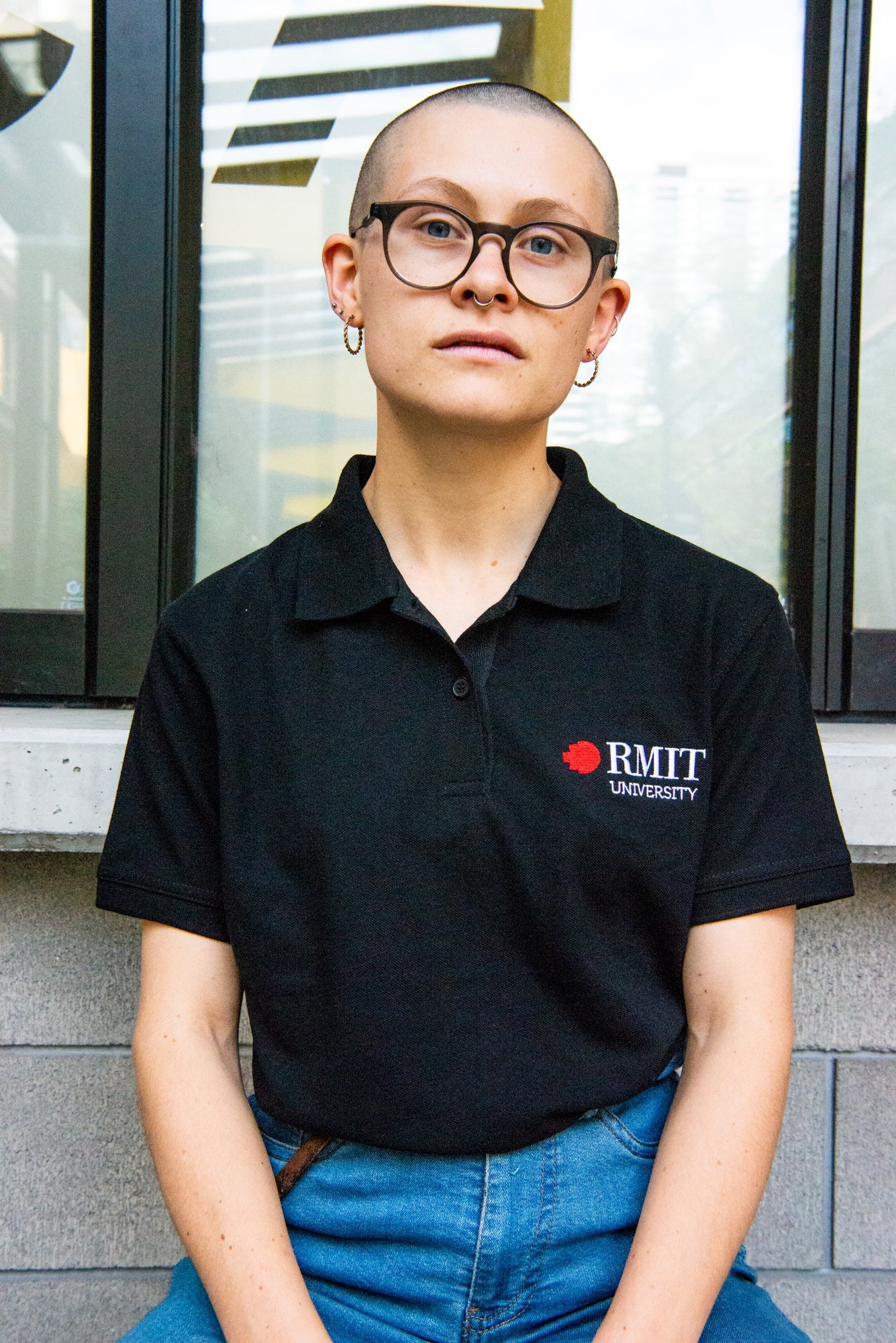 Model wearing a black RMIT Polo featuring the RMIT University logo in red and white, styled with jeans. This polo is commonly used as a uniform, available at the RMIT Store for both casual and professional settings.