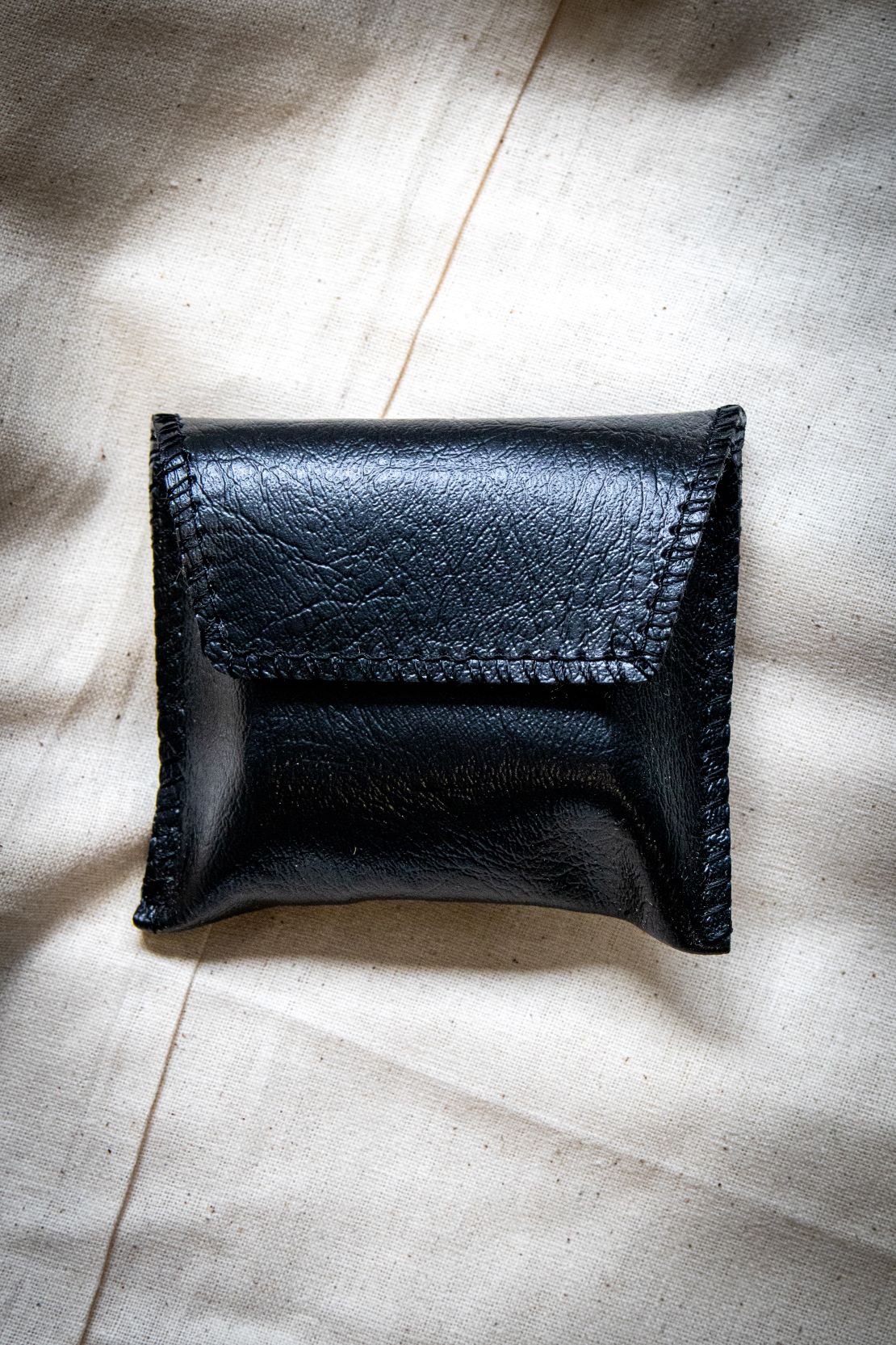 Black pouch for yarn thread counter with a structured button-up lid, made from soft fabric with visible stitching, shown standing upright on a light grey surface. Product for RMIT Store.