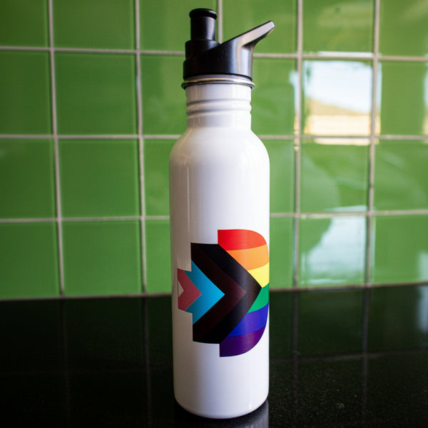Front view of the Progress Pride bottle featuring the Progress Pride flag symbol printed on its white body. The bottle is placed on a black tabletop with a green background. The black cap adds contrast to the clean design. Available at the RMIT Store.