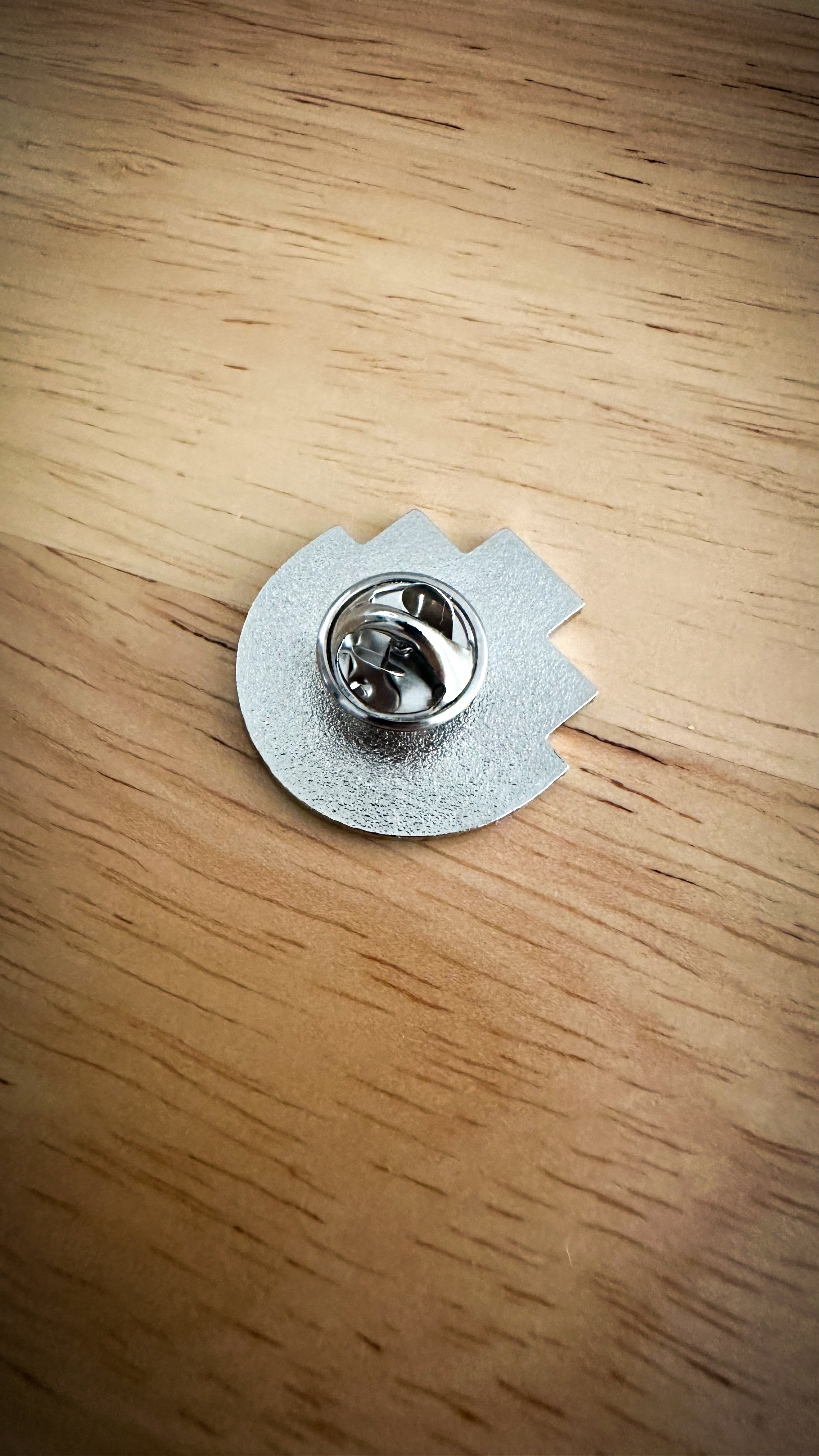 Close-up of the back of a silver metal pronoun pin from the RMIT Store, featuring a butterfly clutch fastener. The metal surface is smooth and reflective.