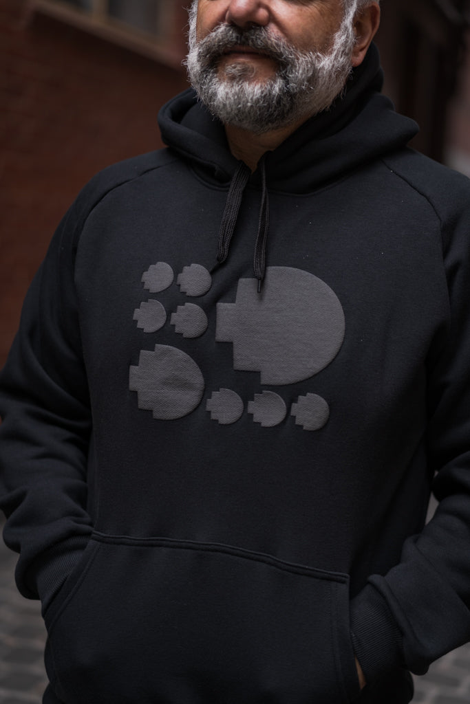 Close-up modelled view of the front of the Puff Pixel Hoodie in black, focusing on the subtle grey pixel pattern design across the chest area. The fabric texture and pixel detailing are clearly visible. Available at RMIT Store.