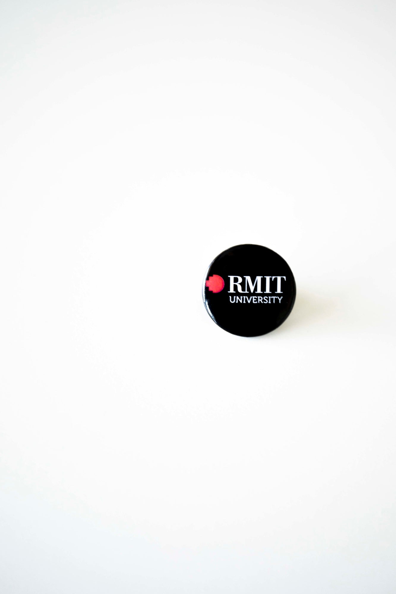 Front view of an RMIT University badge in black. The badge prominently displays the RMIT logo in bold, clear text, suitable for attaching to clothing or accessories.
