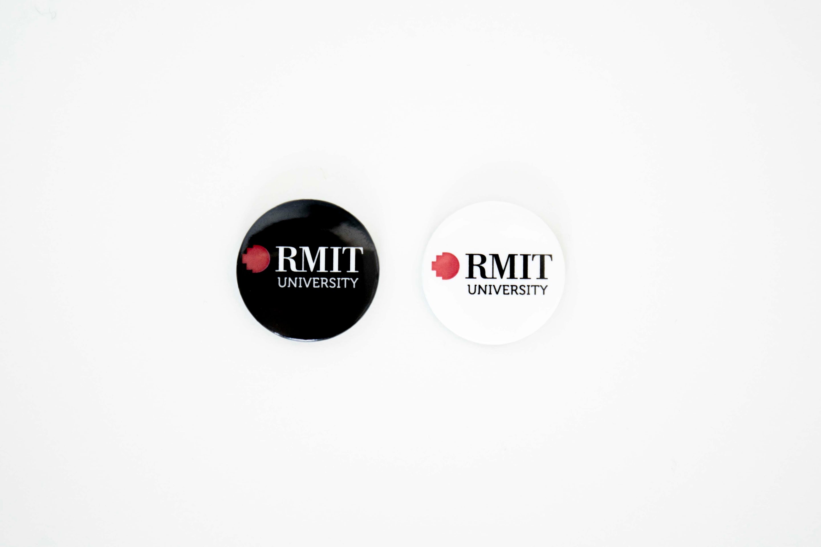 Front view of an RMIT University badge, displaying both black and white variants. The badge features the RMIT logo in a clear, bold design, perfect for use on clothing or accessories.