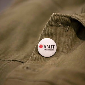 A white RMIT University badge on a green jacket. The badge displays the RMIT logo in white and red, prominently positioned on the left chest area of the jacket.