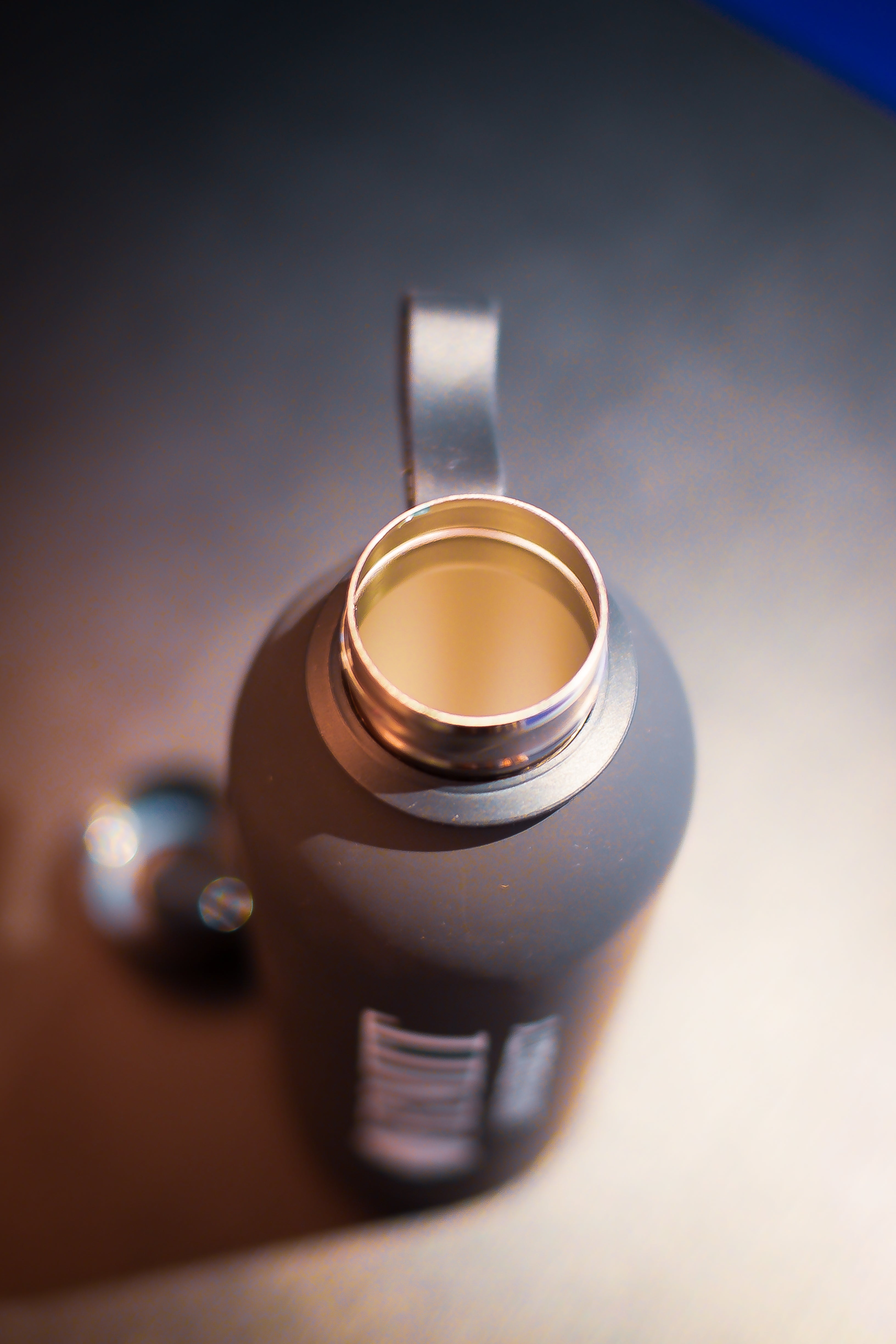 RMIT Everyday Bottle in matte black photographed from above at RMIT Store, showing open stainless steel mouth with threaded rim, smooth interior lining, attached carry loop strap, and softly blurred hand and background elements.