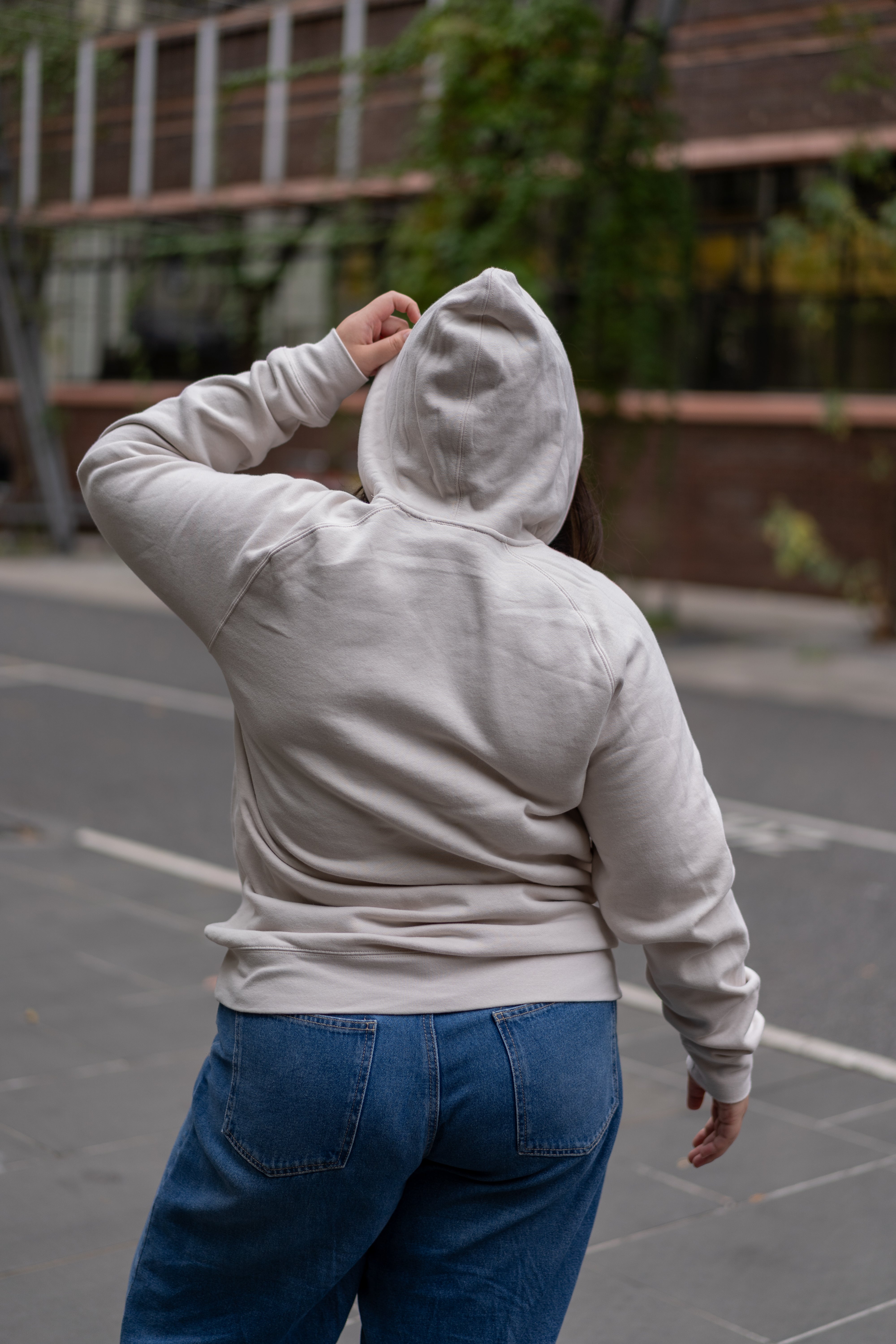 Rear view of model wearing the RMIT Store Limited Edition Bone Hoodie, highlighting the plain back, structured hood, and soft premium cotton fabric in a natural outdoor setting.