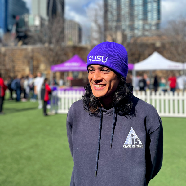 A smiling model wearing the Purple RUSU Beanie with white embroidered logo in an outdoor setting, available at the RMIT Store.